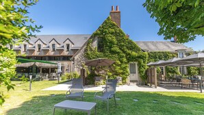 Une cour avec des sièges en plein air, un bâtiment doté d’une cheminée et des murs recouverts de lierre.