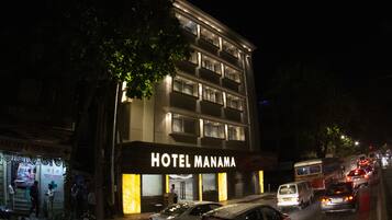 A hotel with multiple floors, a prominent sign, and a street with parked cars and a bus.
