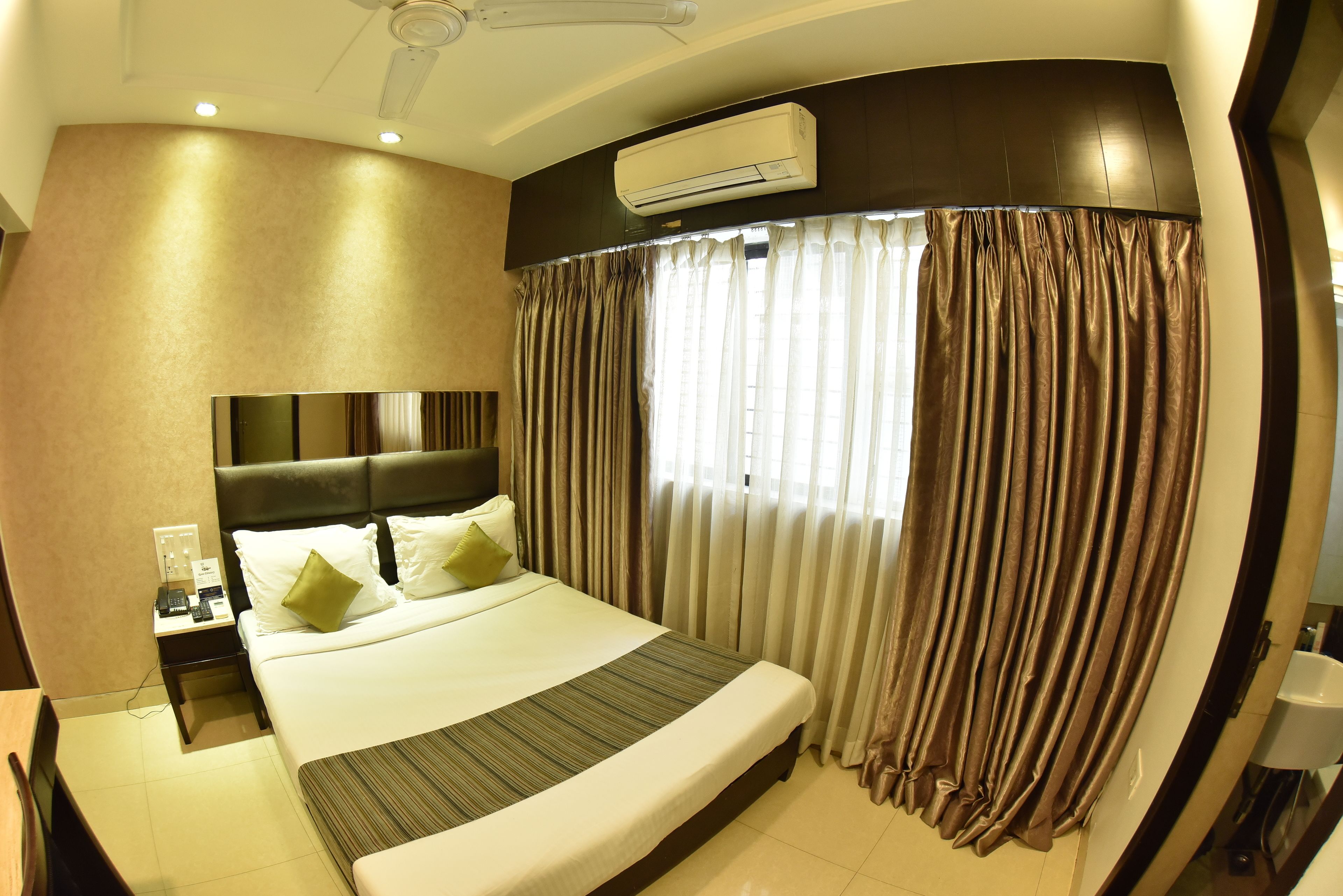 A hotel room with a large bed, a headboard, an air conditioning unit, a nightstand, and a window with curtains.
