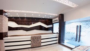 A modern reception area with a curved reception desk, a patterned wall, and a glass door leading outside. - Hotel Manama (Mumbai)