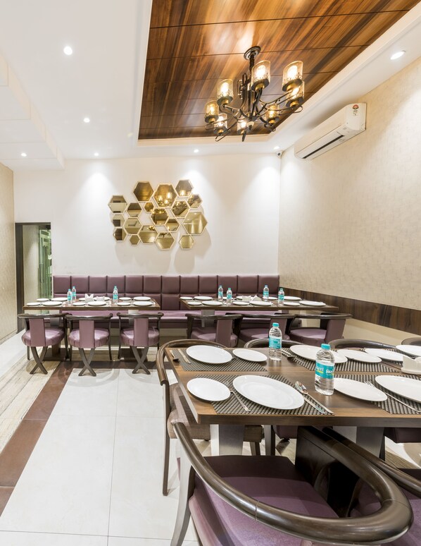 A conference room with a long table, purple cushioned seating, and a chandelier. - Hotel Manama (Mumbai)