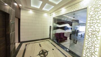 A modern lobby with a geometric floor design, a glass partition with a purple chair, and a ceiling with recessed lighting.