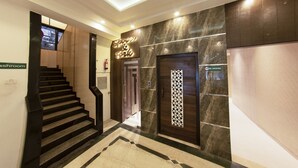 A modern hotel lobby with a marble staircase, a 'Spice & Fork' sign, a 'No Smoking' sign, and a 'Restroom' sign. - Hotel Manama (Mumbai)