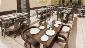 A spacious dining area with multiple tables and chairs, a chandelier, and a modern ceiling design. - Hotel Manama (Mumbai)