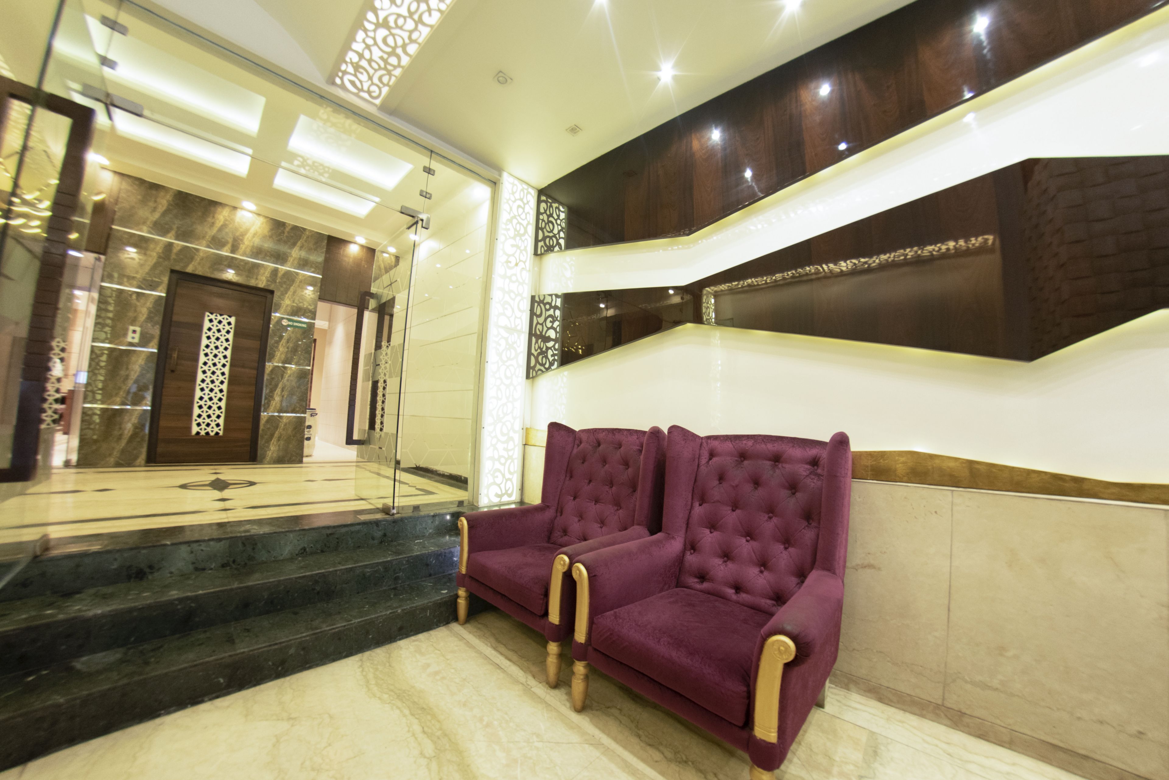 A lobby with a marble staircase, a purple sofa, and a decorative wall.