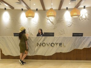 A reception desk with 'NOVOTEL' branding, a receptionist, and a guest. - Novotel Cairo El Borg (Cairo)