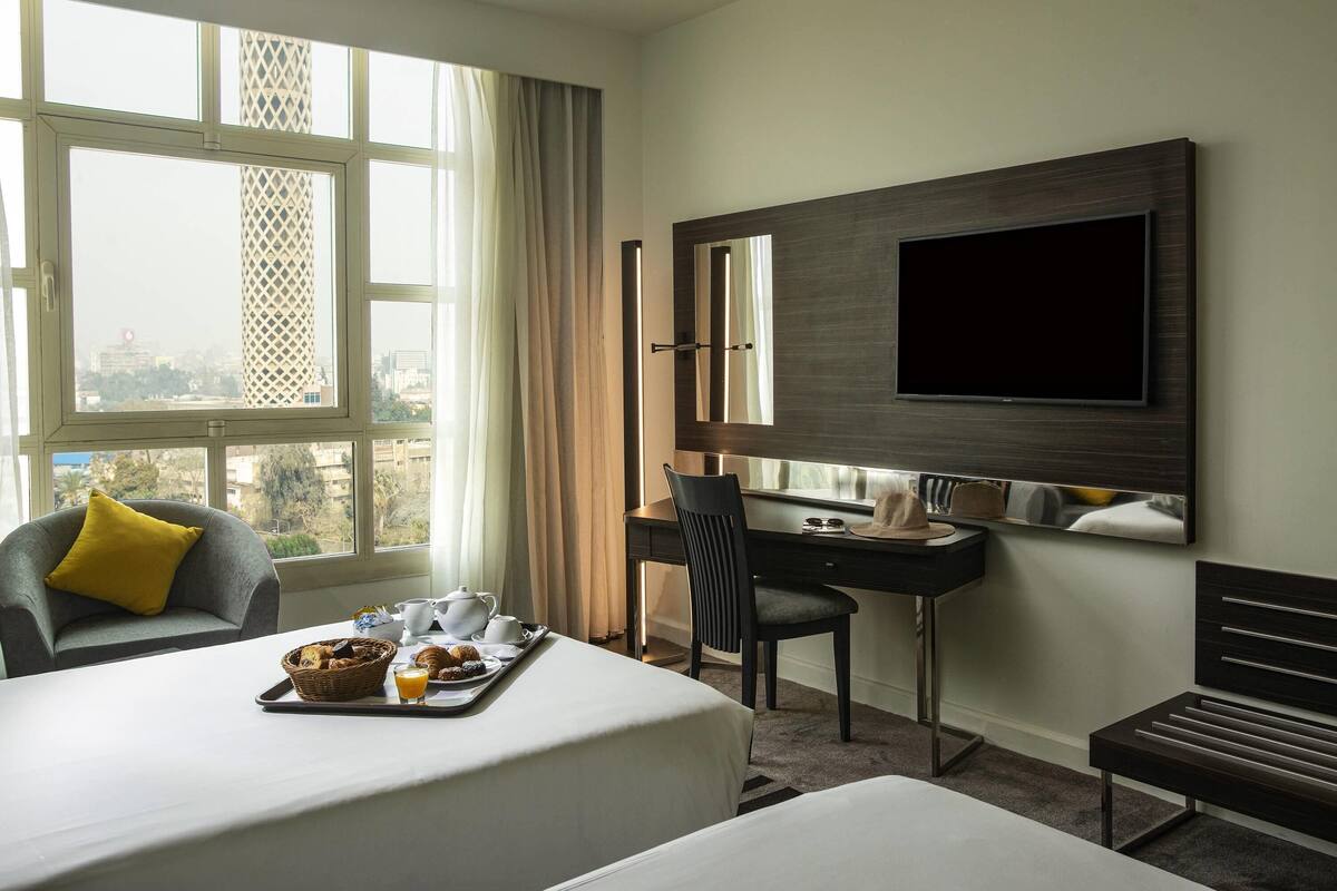 A hotel room with a bed, a desk, a chair, a TV, and a window with a city view.