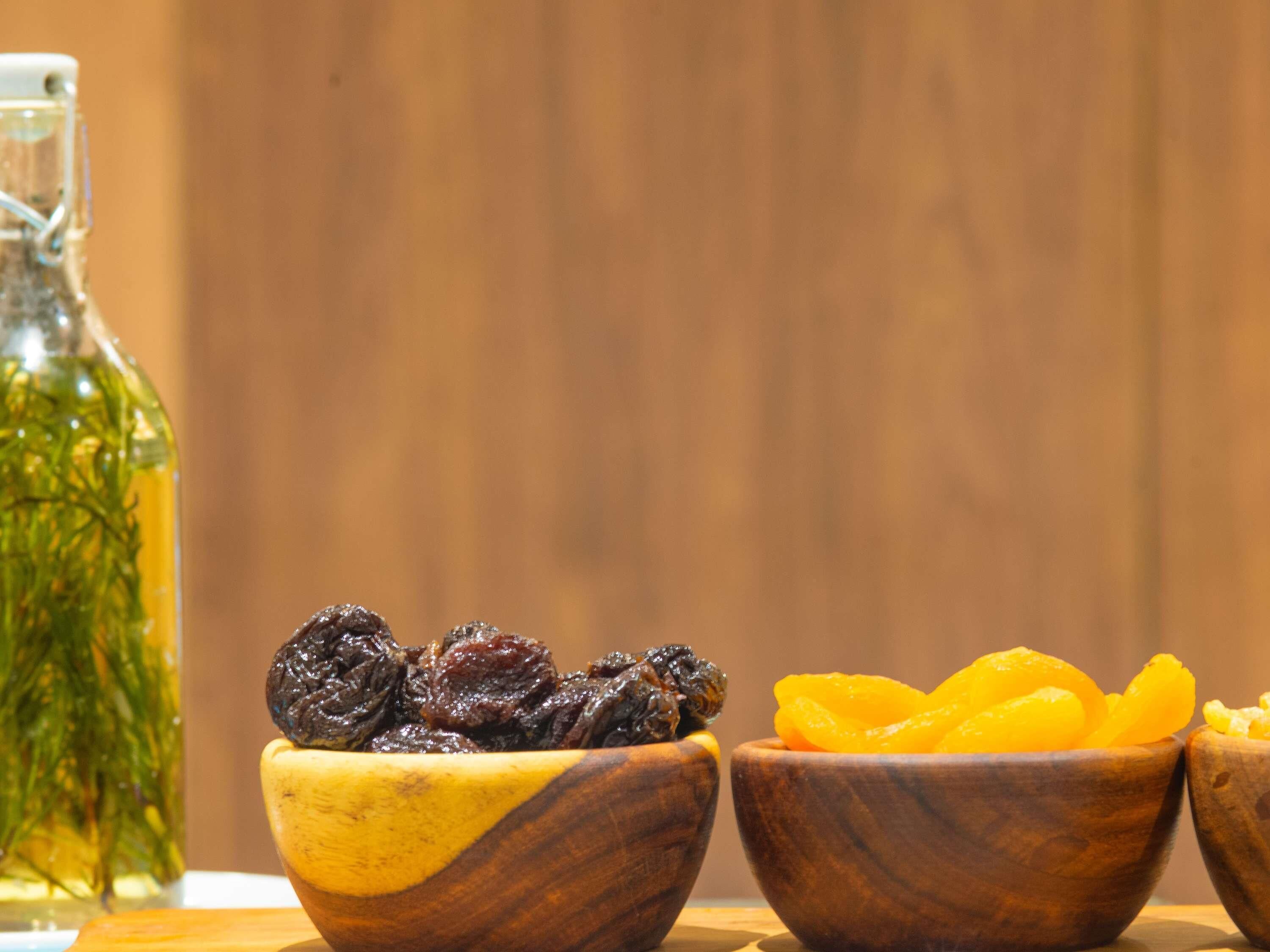 Tres cuencos de madera con frutas secas, una botella de líquido verde y un fondo de madera.