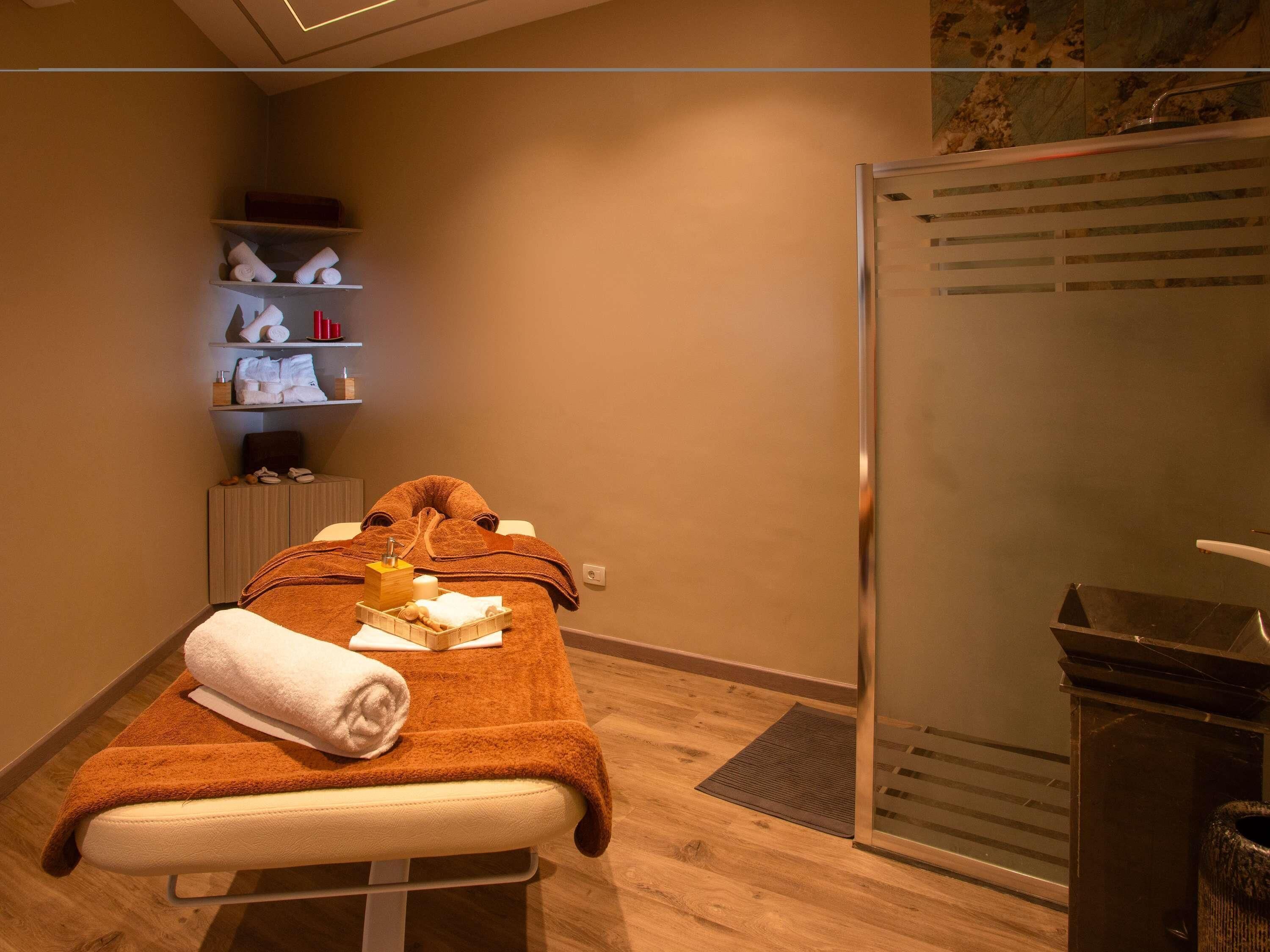 Una mesa para masajes con toallas, una botella y una bandeja de objetos en un spa con estanterías al fondo.