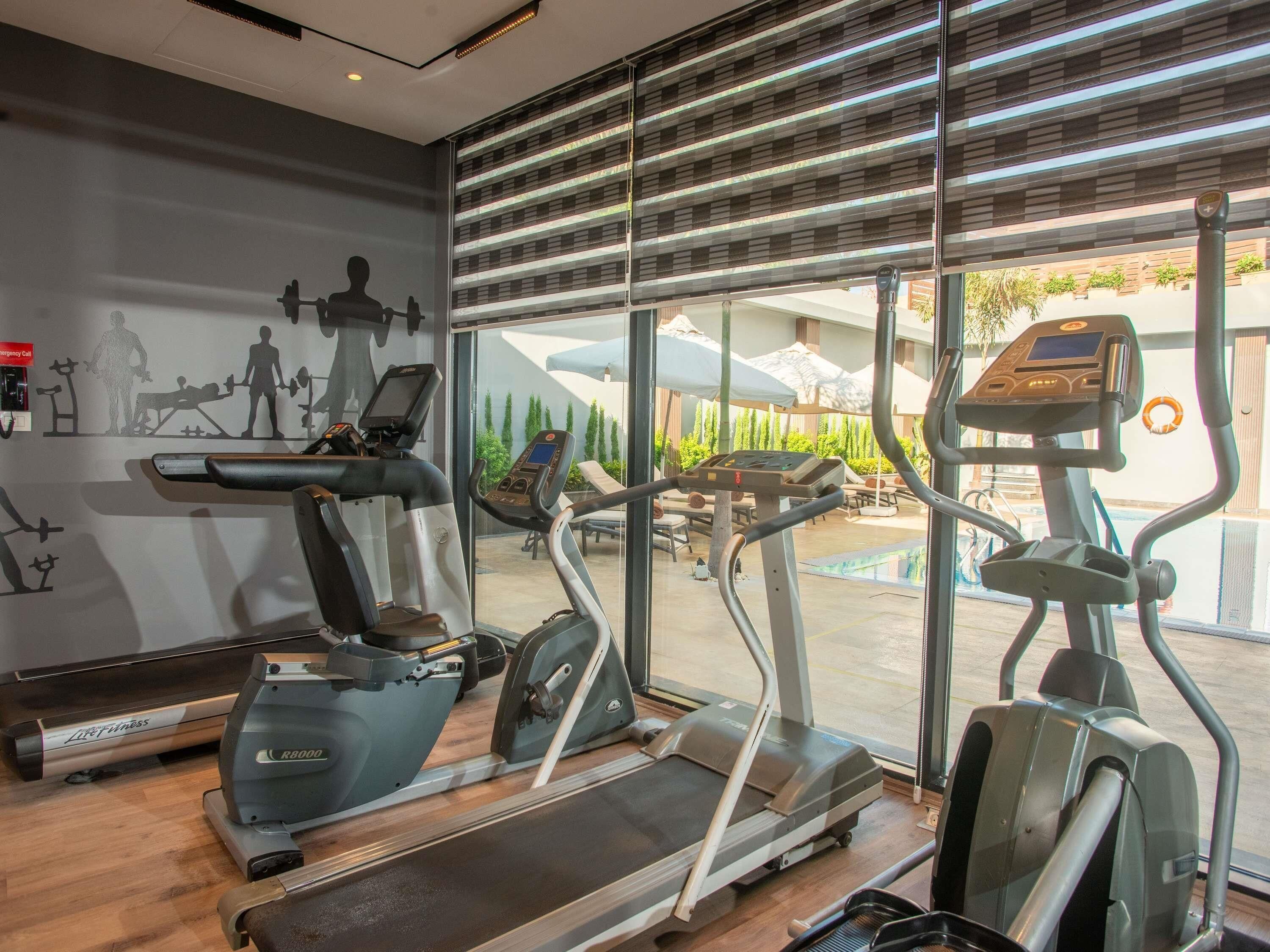 A gym with treadmills, elliptical machines, and a wall with fitness silhouettes.