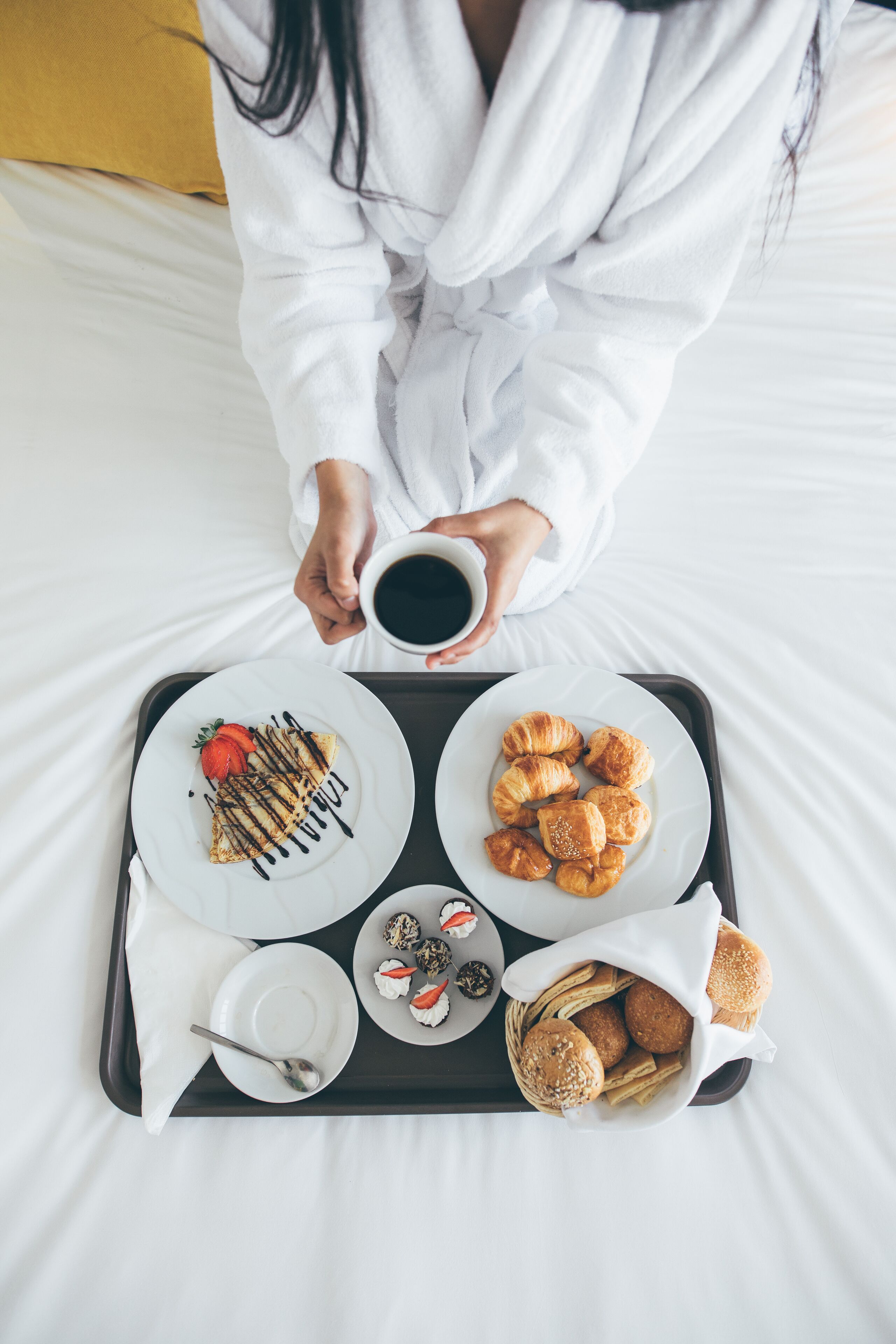 Bandeja de desayuno con cruasanes, gofres y pasteles sobre una cama.