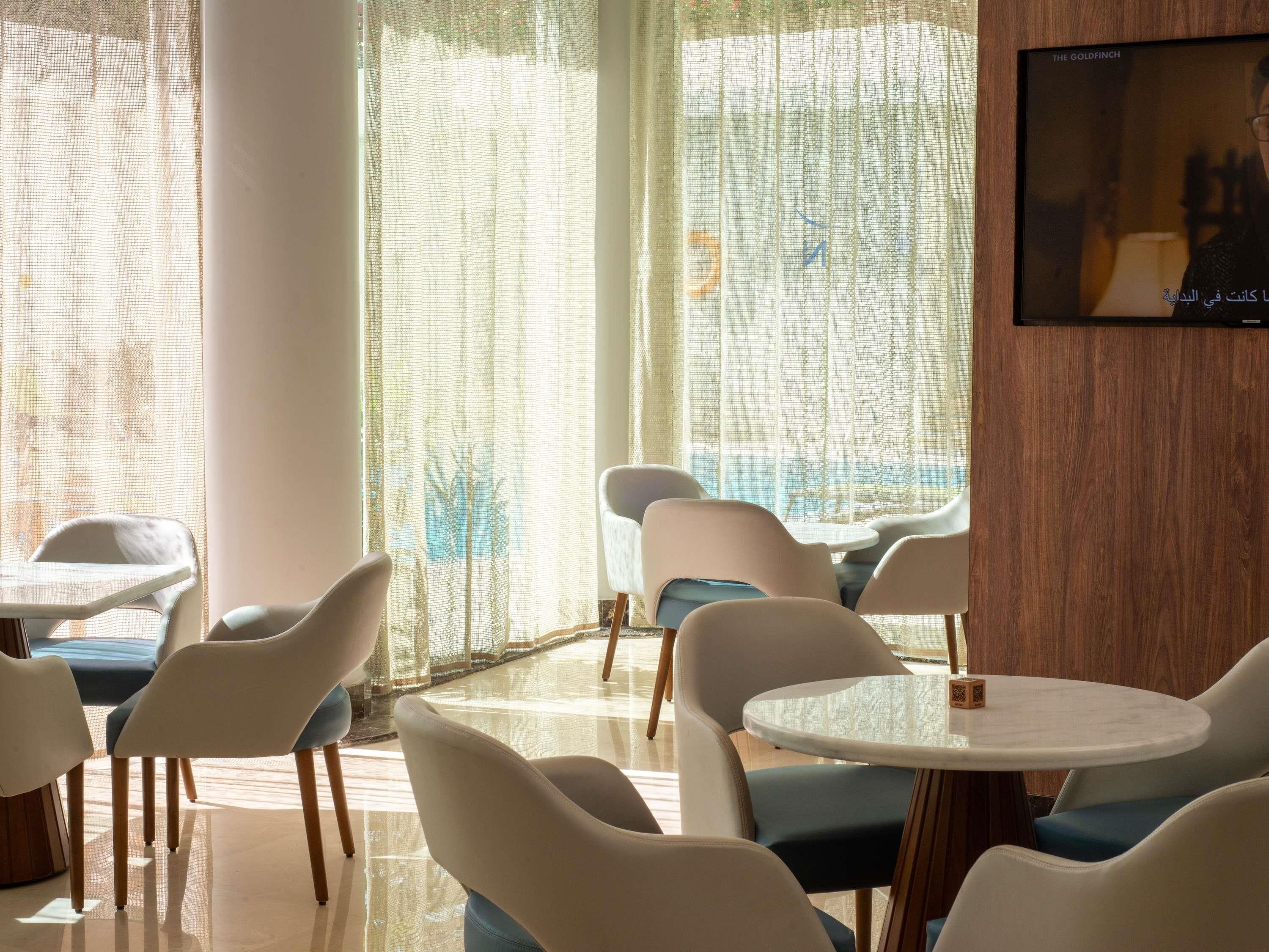 A modern hotel room with a large window, a flat-screen TV, and a round table with chairs.