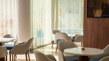 A modern hotel room with a large window, a flat-screen TV, and a round table with chairs.