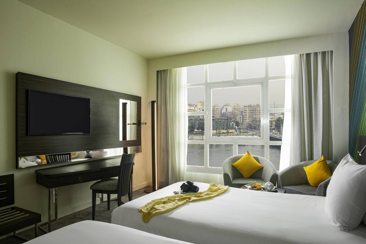 A hotel room with a bed, a desk, a chair, a television, and a window with a city view.