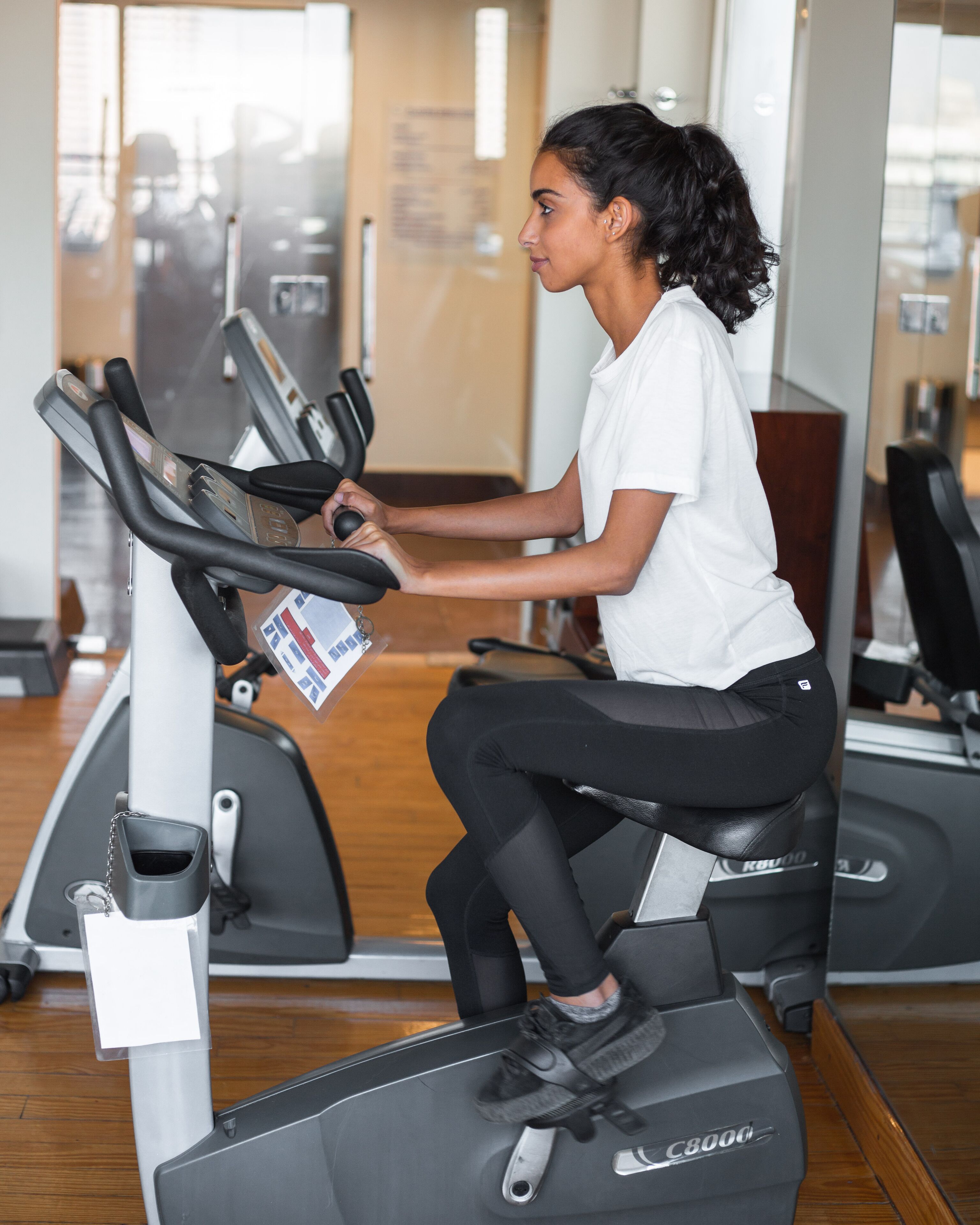 A person using a treadmill in a gym with a mirrored wall and wooden flooring.