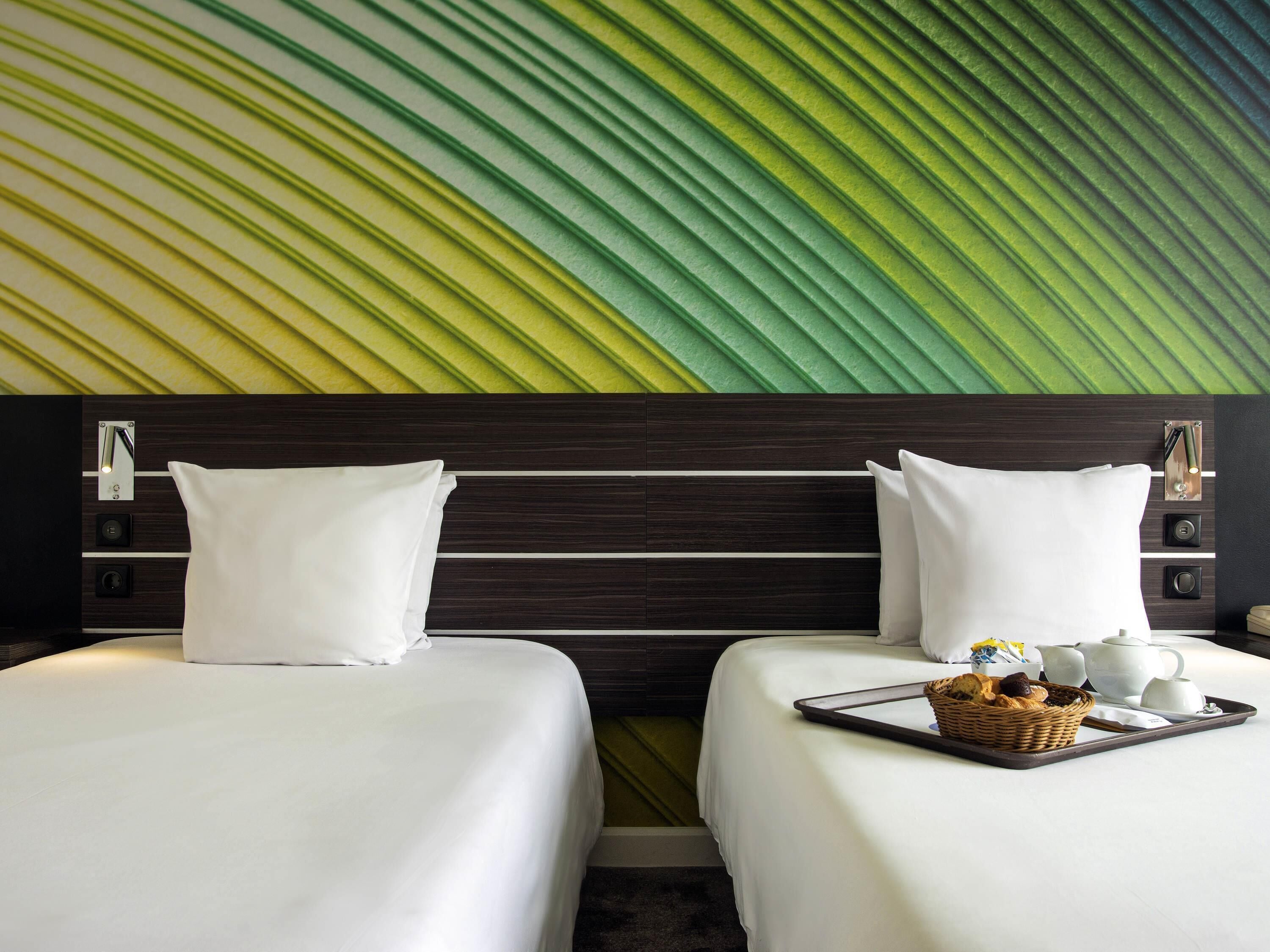 A hotel room with two beds, a wall with a leaf pattern, and a tray with breakfast items.