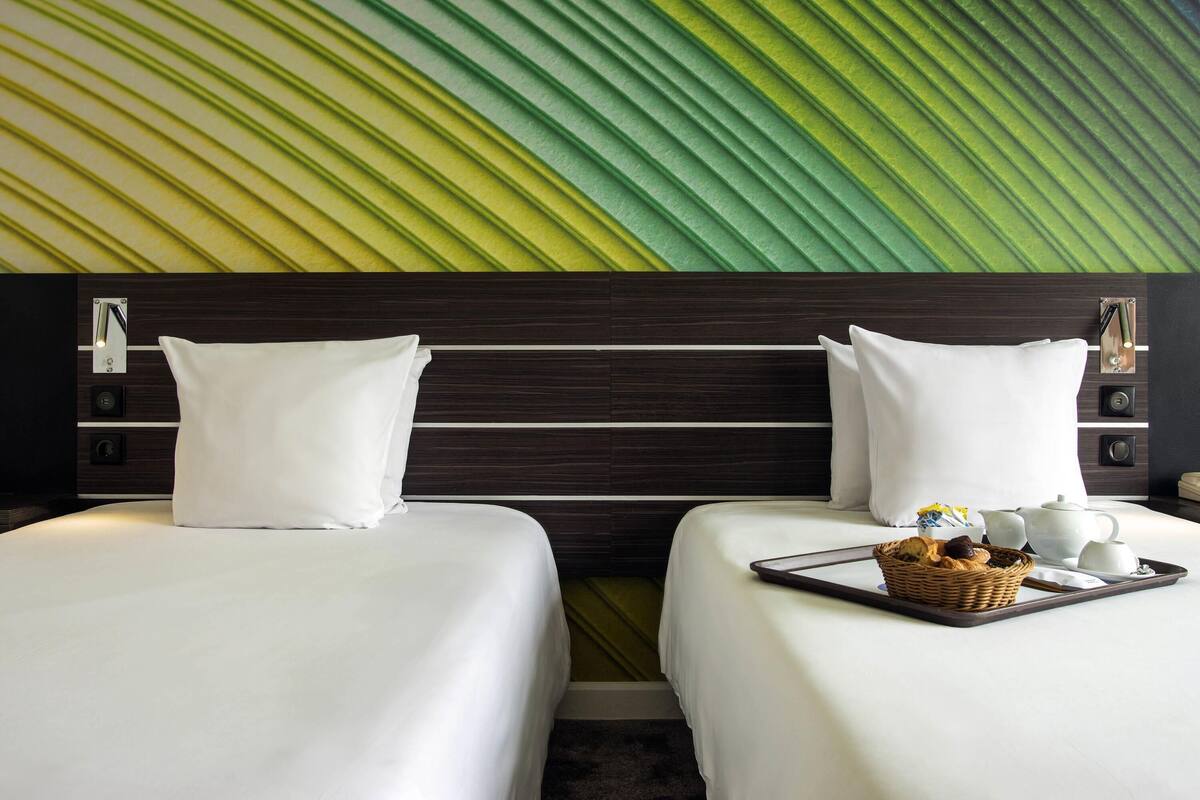 A hotel room with two beds, a wall with a leaf pattern, and a tray with breakfast items.