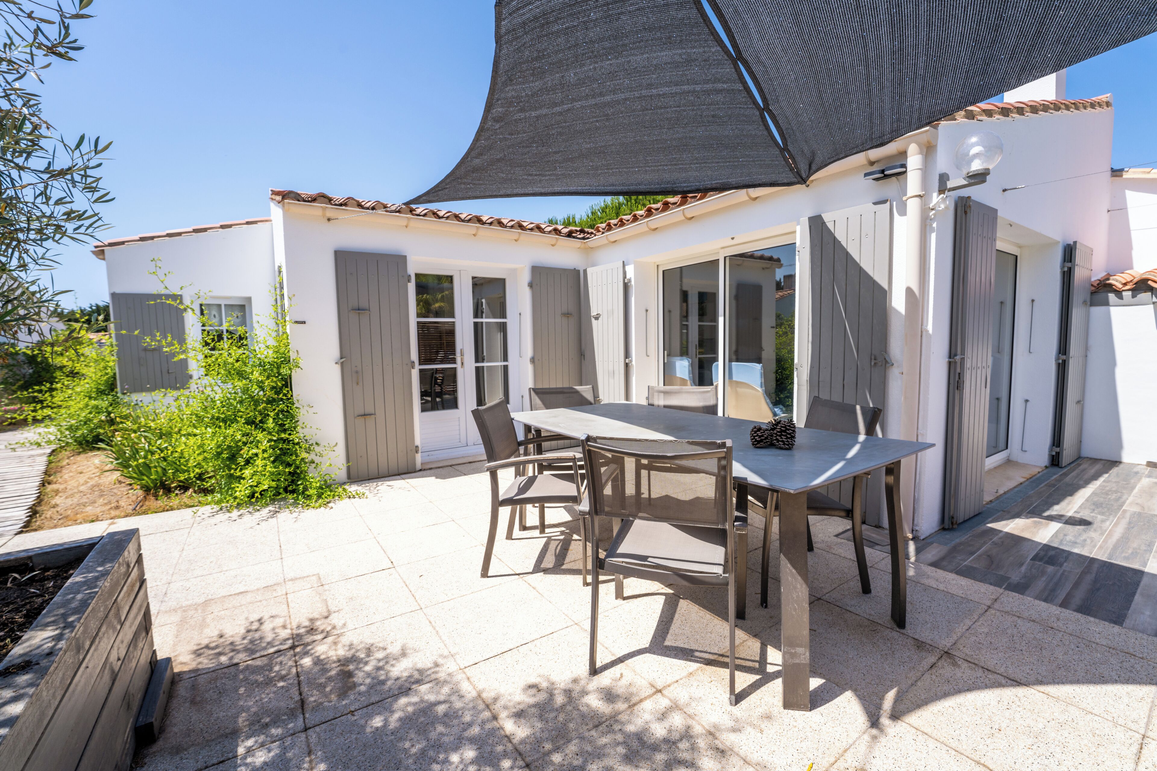 Eine Terrasse mit Tisch und Stühlen, einer Pergola und einem weiß gestrichenen Gebäude mit Fensterläden.