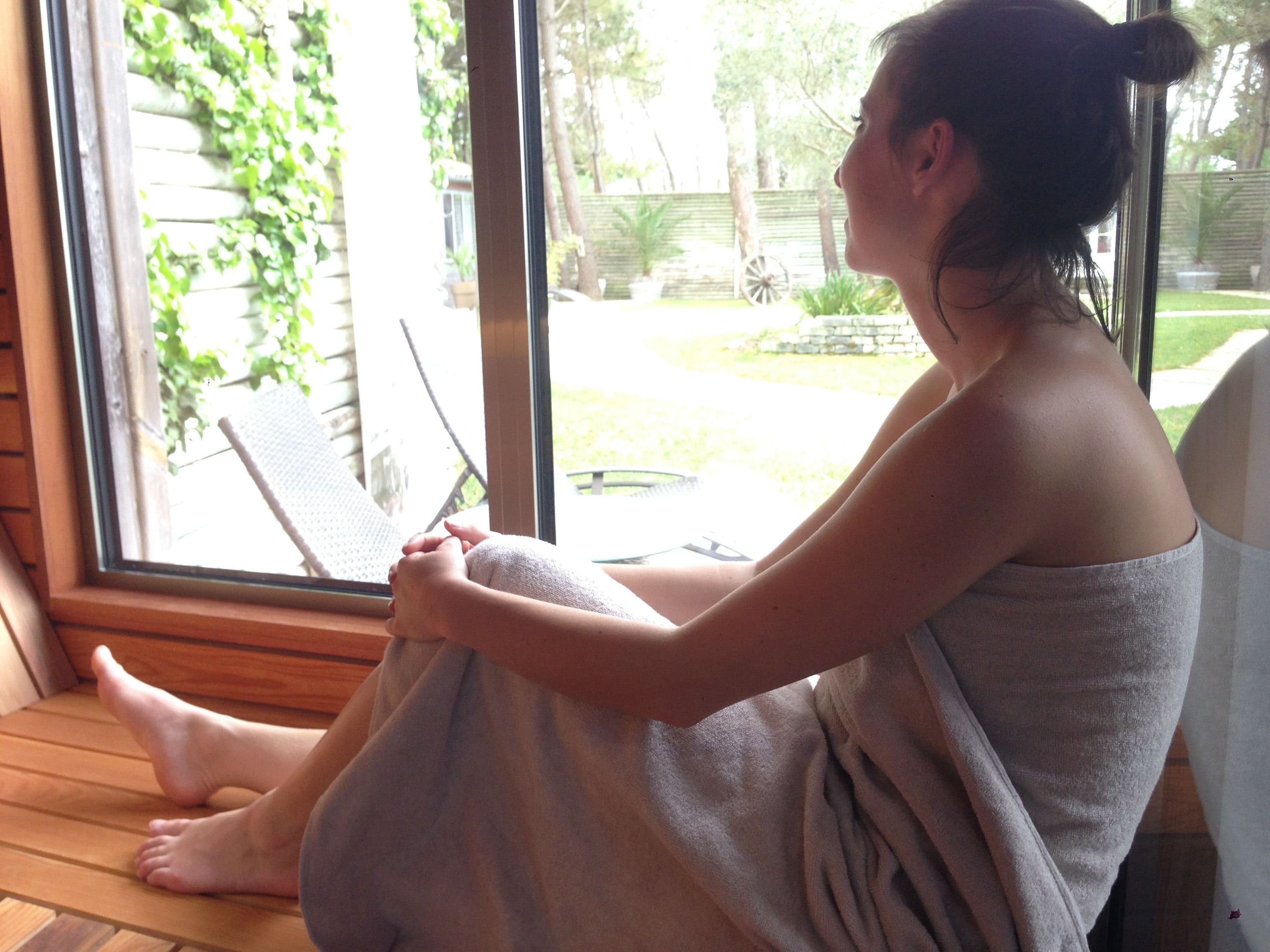 A person sitting by a window with a view of a garden and a wooden deck.