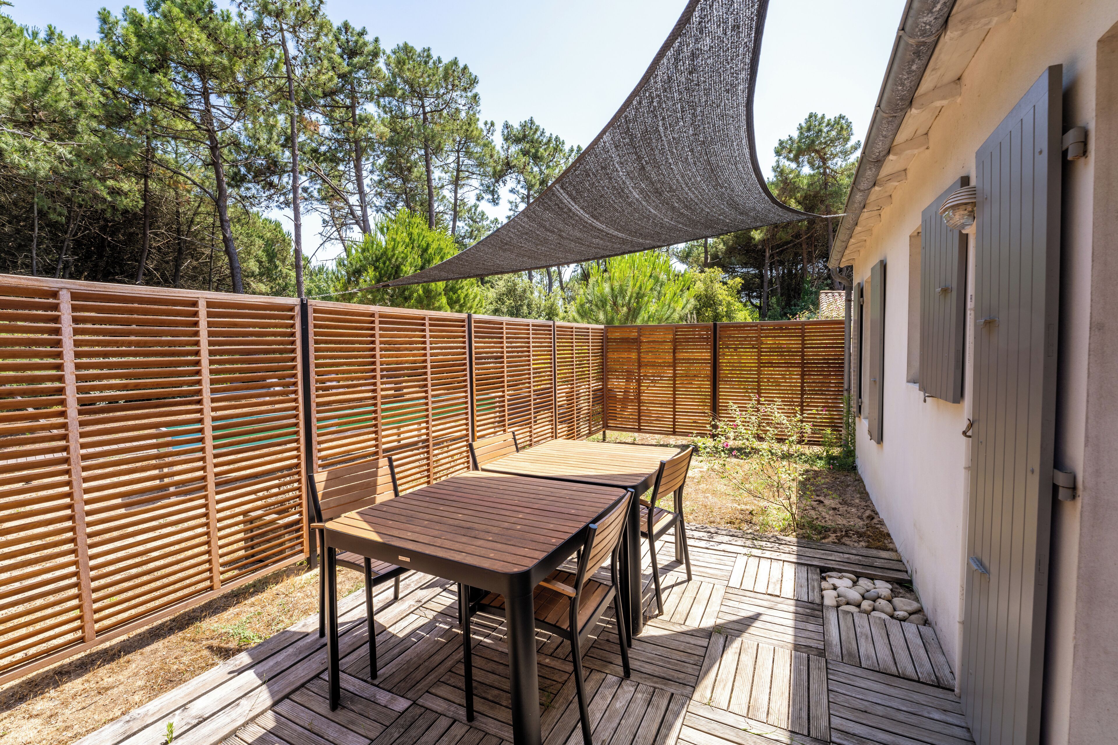 A wooden deck with a table and chairs, surrounded by a wooden fence and a shaded area.