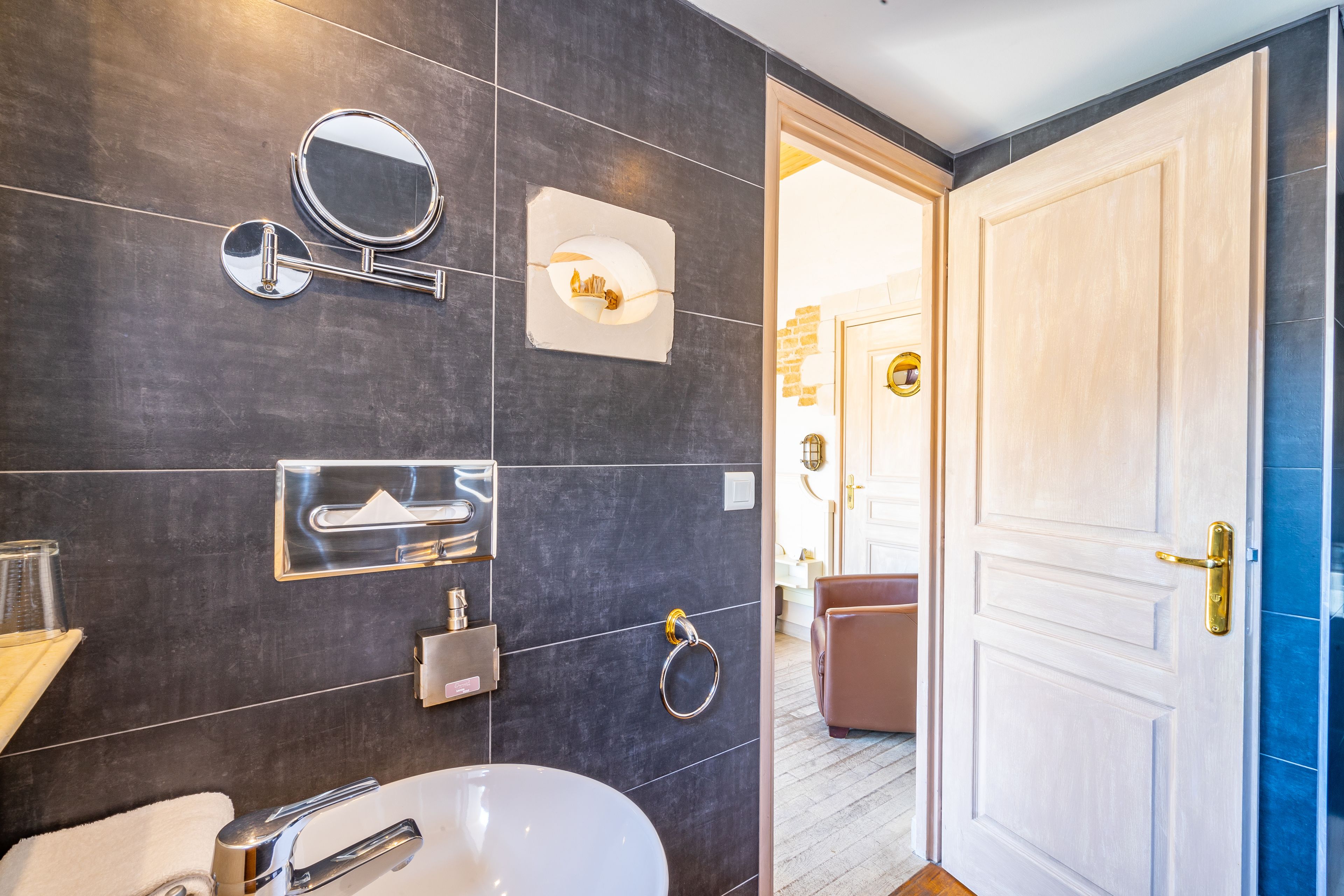Ein modernes Badezimmer mit dunklen Fliesen, einem weißen Waschbecken, einem Spiegel und einem Handtuchhalter.