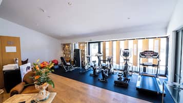 Et rummeligt fitnesscenter med forskellig træningsudstyr, en receptionsdisk og store vinduer der lukker naturligt lys ind.