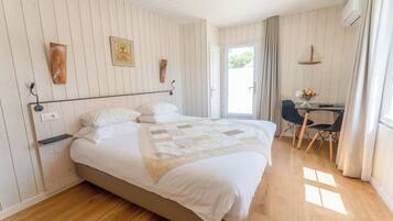 A bedroom with a bed, bedside tables, a desk with a chair, and a door leading to an outdoor area.