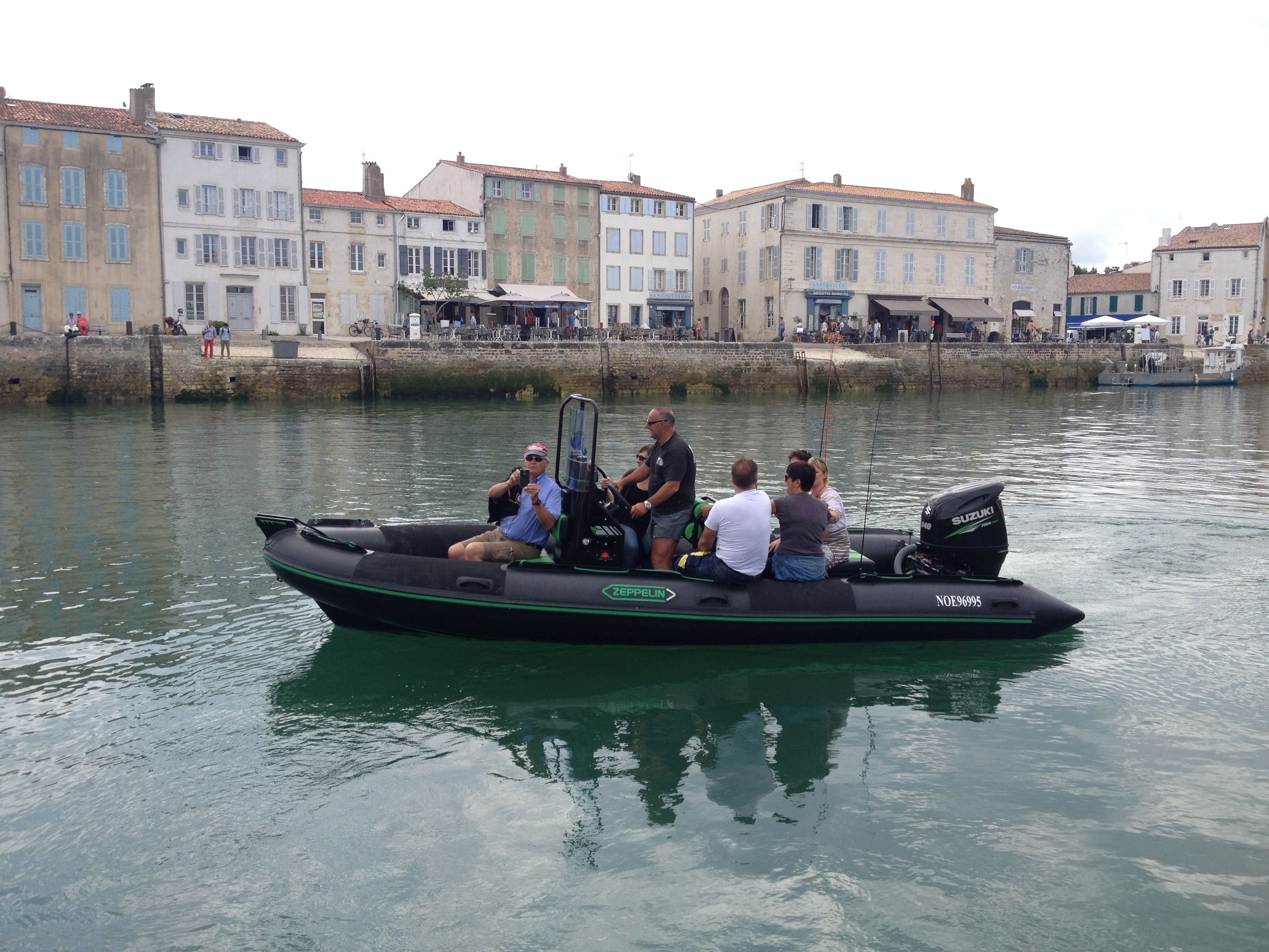 A small motorboat with several people on it, docked near a waterfront with buildings in the background.