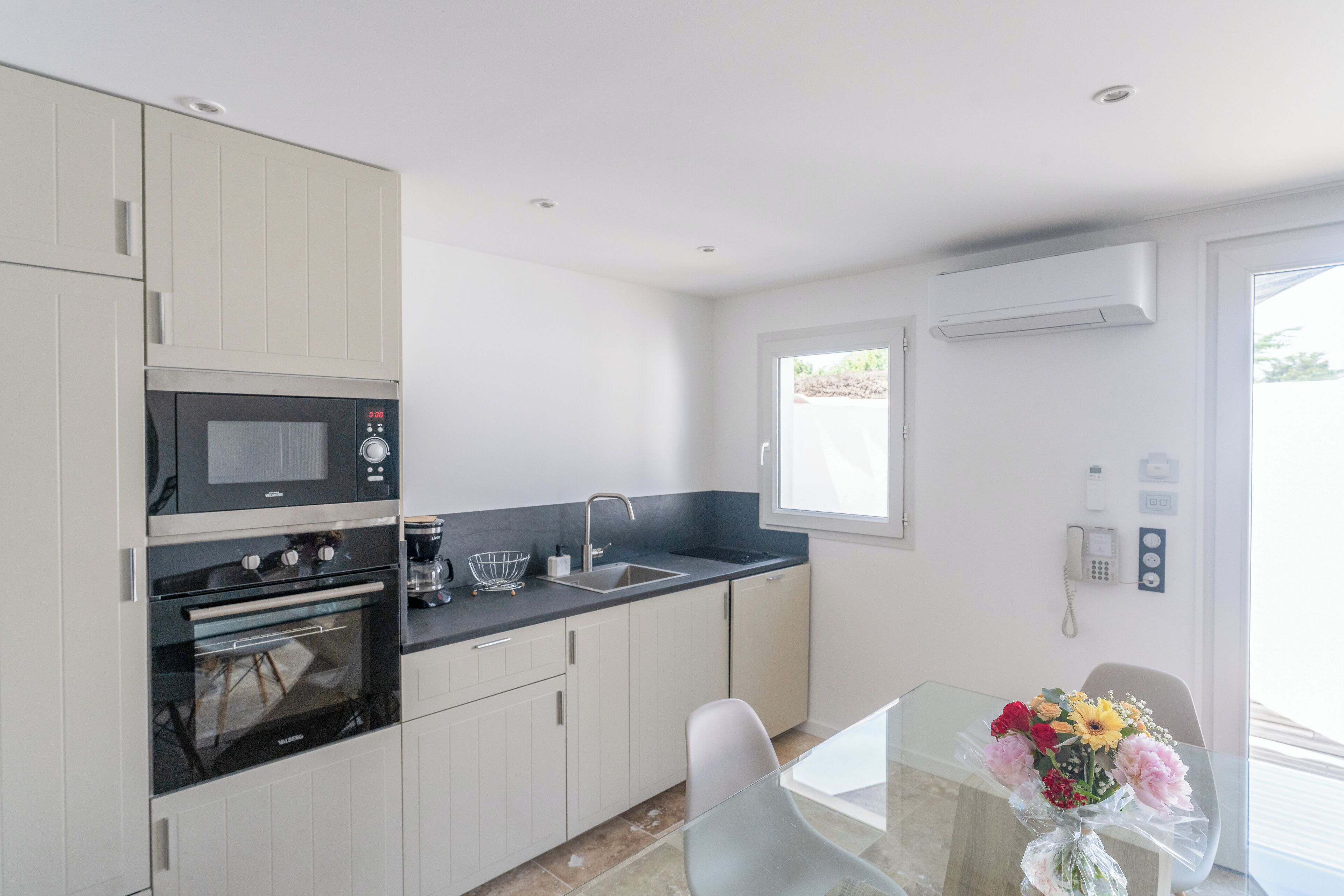 A modern kitchen with built-in appliances, a glass dining table, and a window with a view.