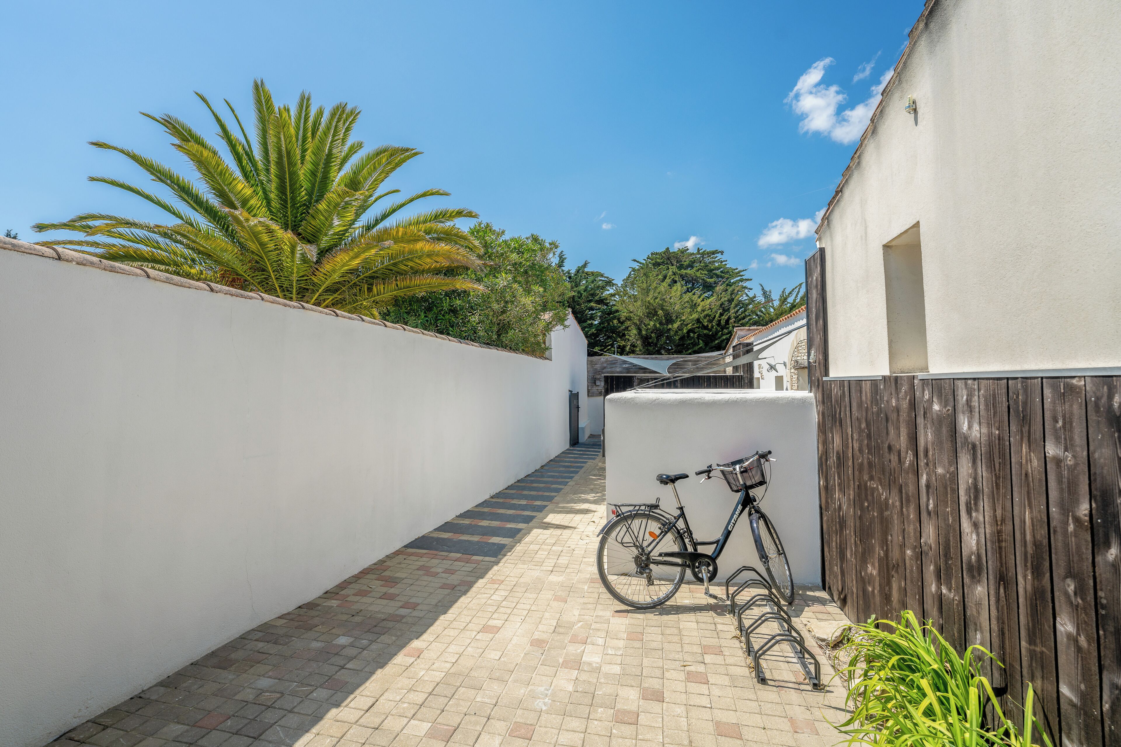 A narrow alleyway with a bicycle parked against a white wall, leading to a building with a wooden fence.