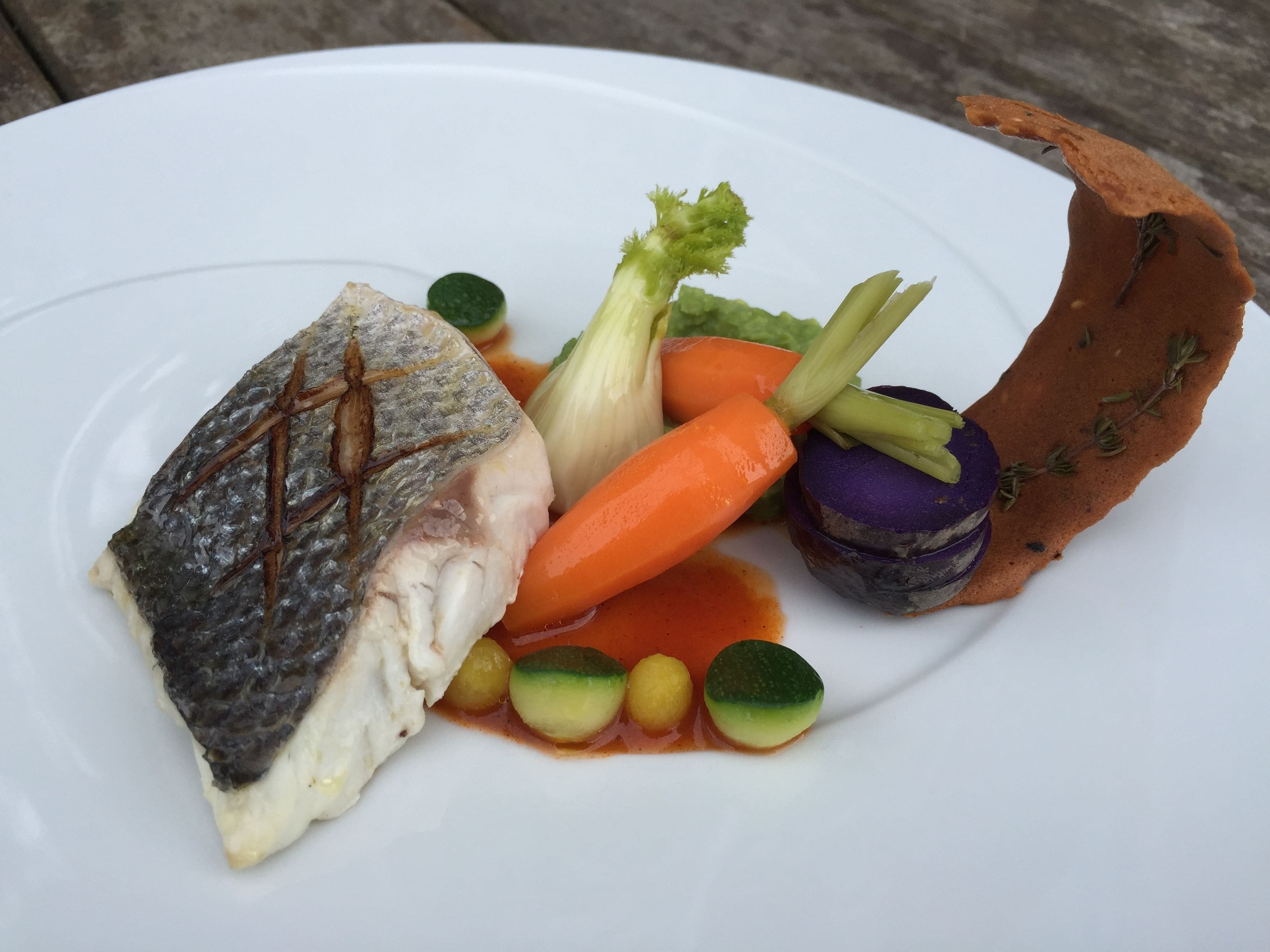 Une assiette blanche contenant du poisson, des légumes et une sauce.