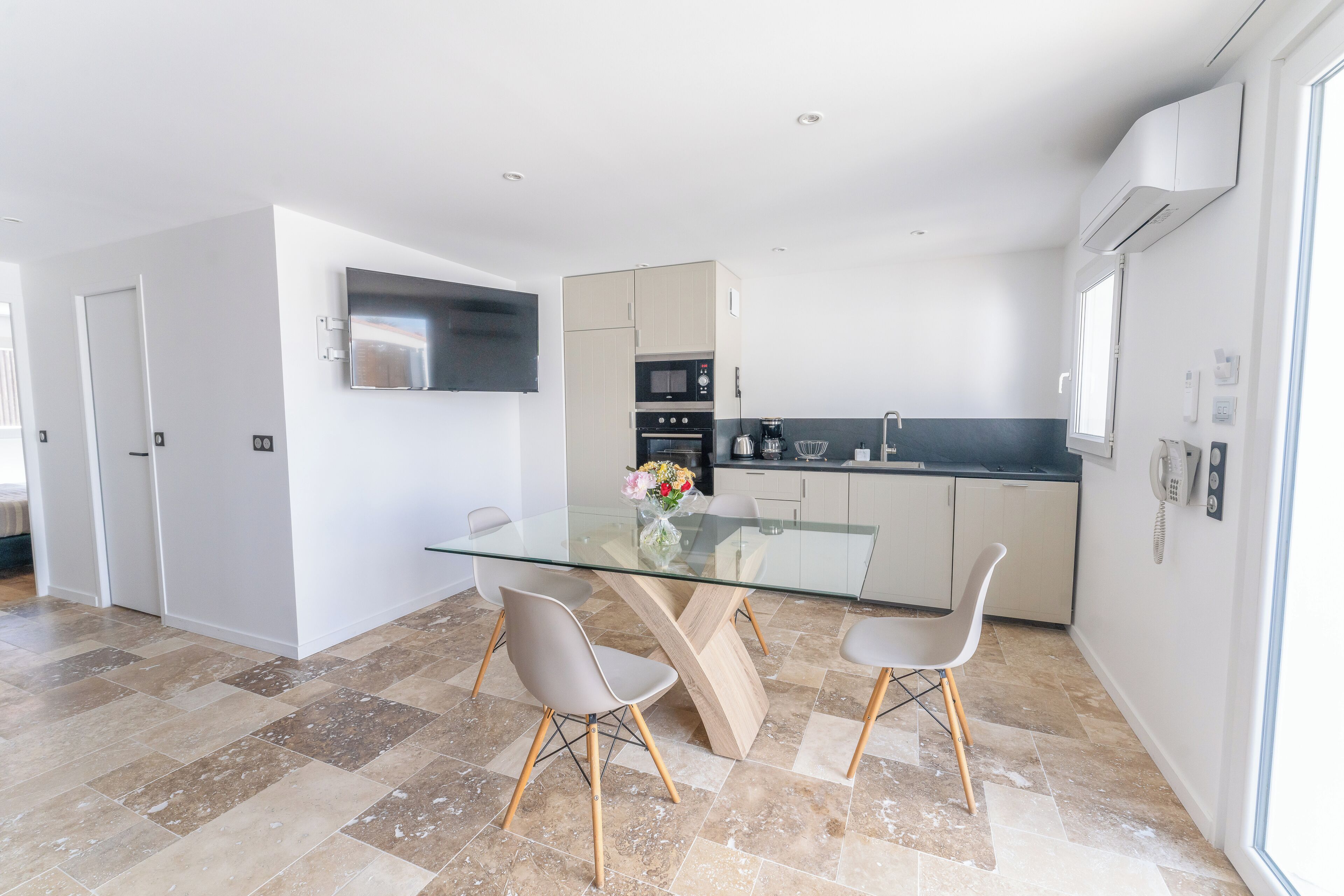 A modern kitchen with a glass dining table, two chairs, and a built-in oven.