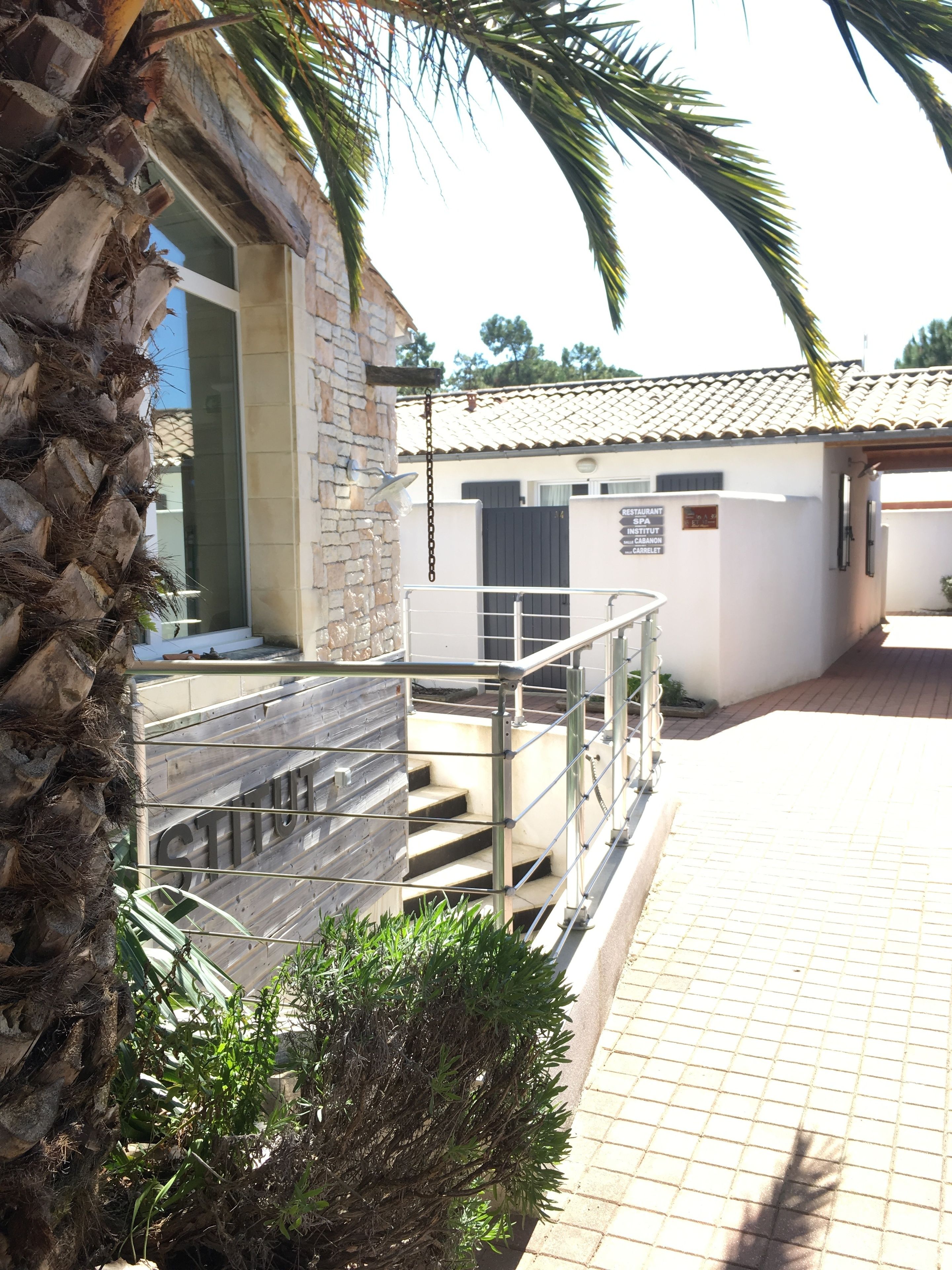 A building with a staircase leading to a covered area, a palm tree, and a sign indicating a restaurant, spa, and institute.