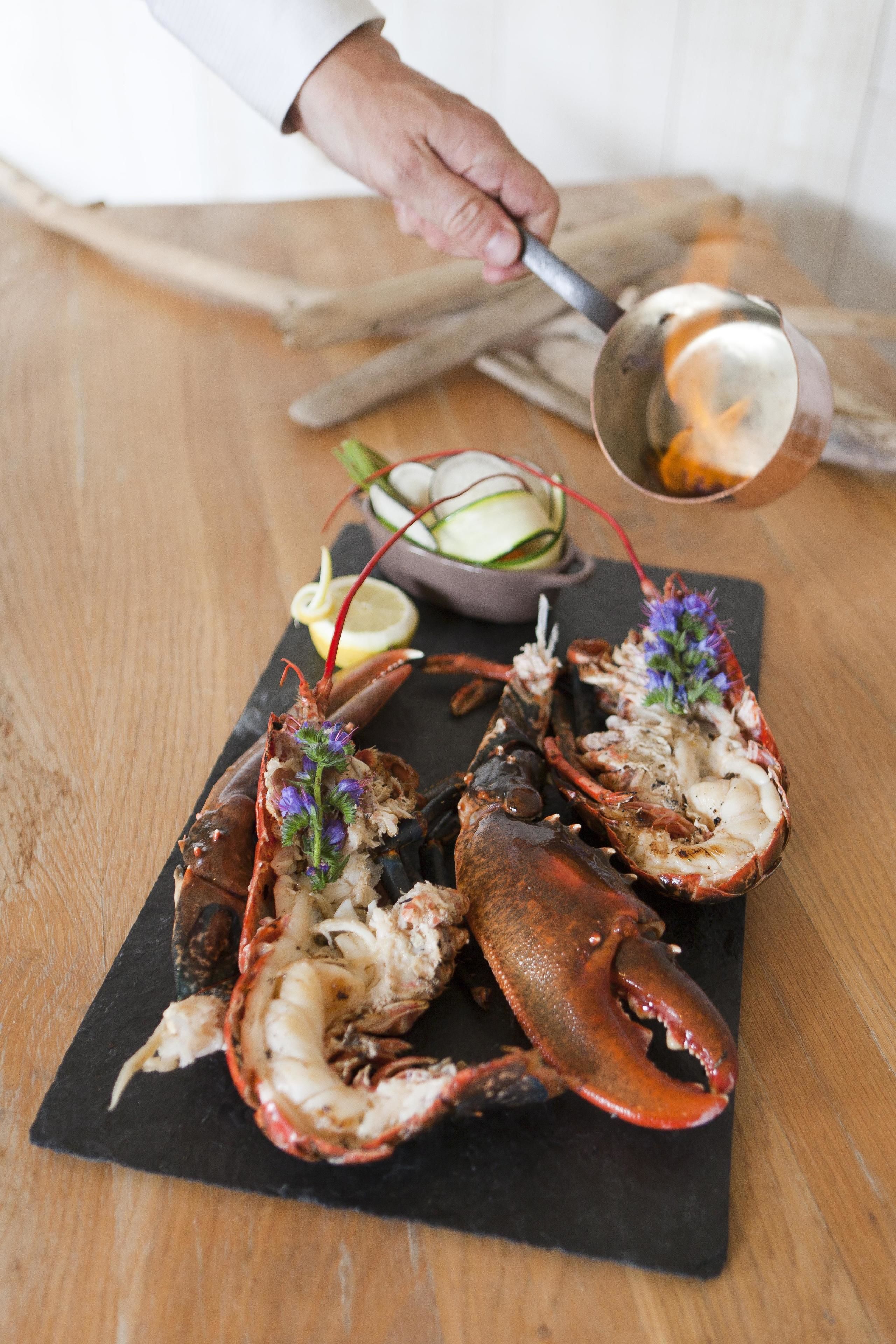 A lobster on a black slate board with a lemon wedge and a small bowl of sauce.