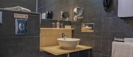 Une salle de bain moderne avec des carreaux foncés, un plancher en bois, un lavabo blanc, des toilettes et un miroir.