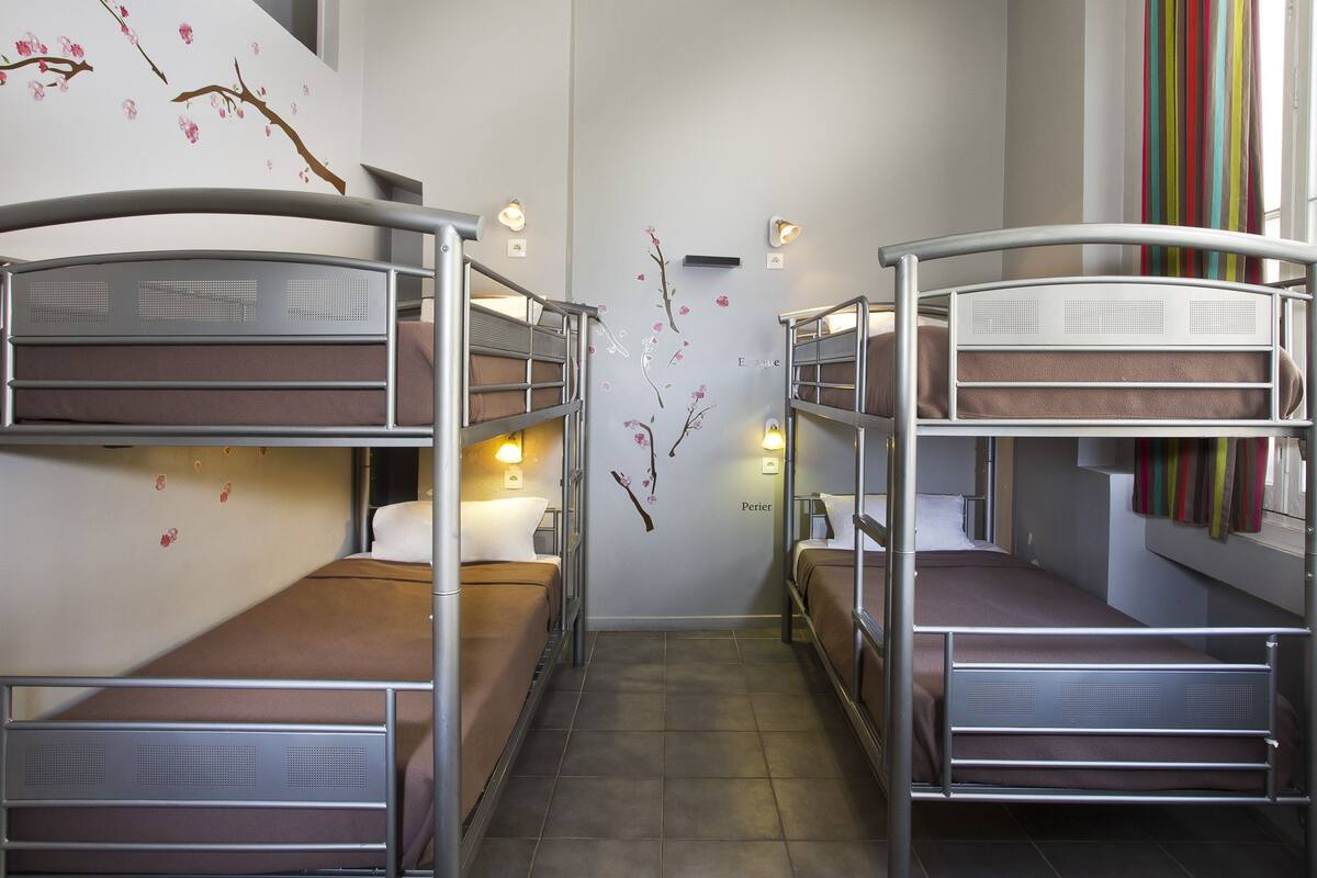 A narrow corridor with bunk beds on either side, a wall-mounted light fixture, and a window with a striped curtain.