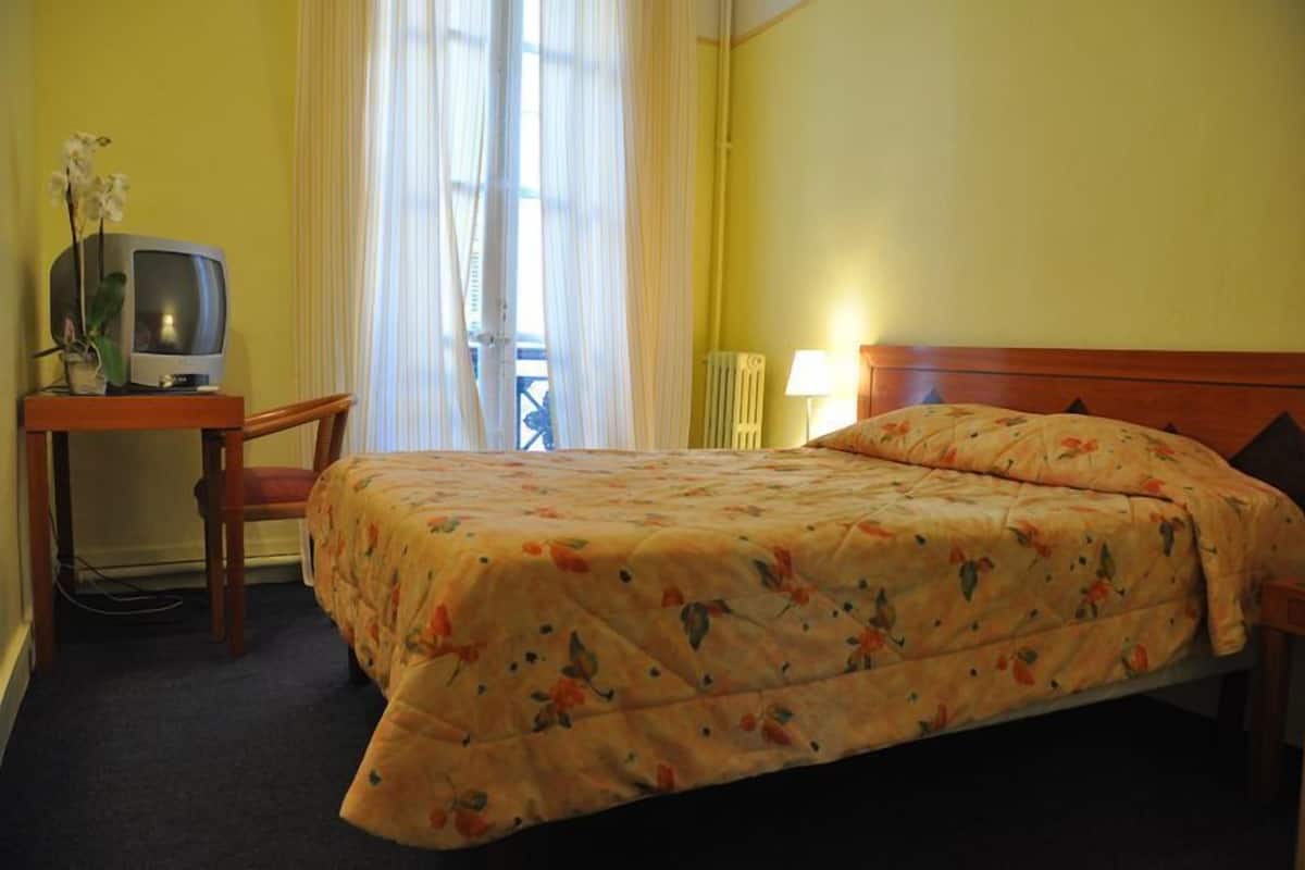 A hotel room with a bed, a desk with a television, and a window with curtains.
