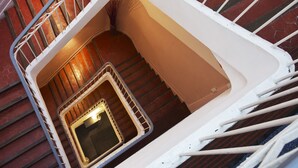 A spiral staircase with a metal railing, a small window, and a door at the bottom. - Hotel Sylvabelle (Marseille)