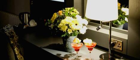 Un'area reception con schermo di benvenuto, un tavolo con lampada, fiori e due bicchieri.