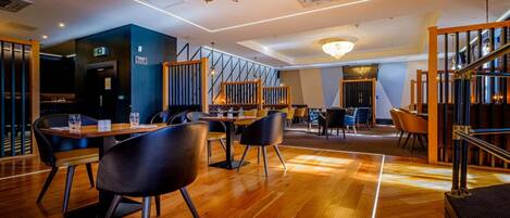 Un restaurante moderno con suelo de madera, sillas negras y un candelabro.
