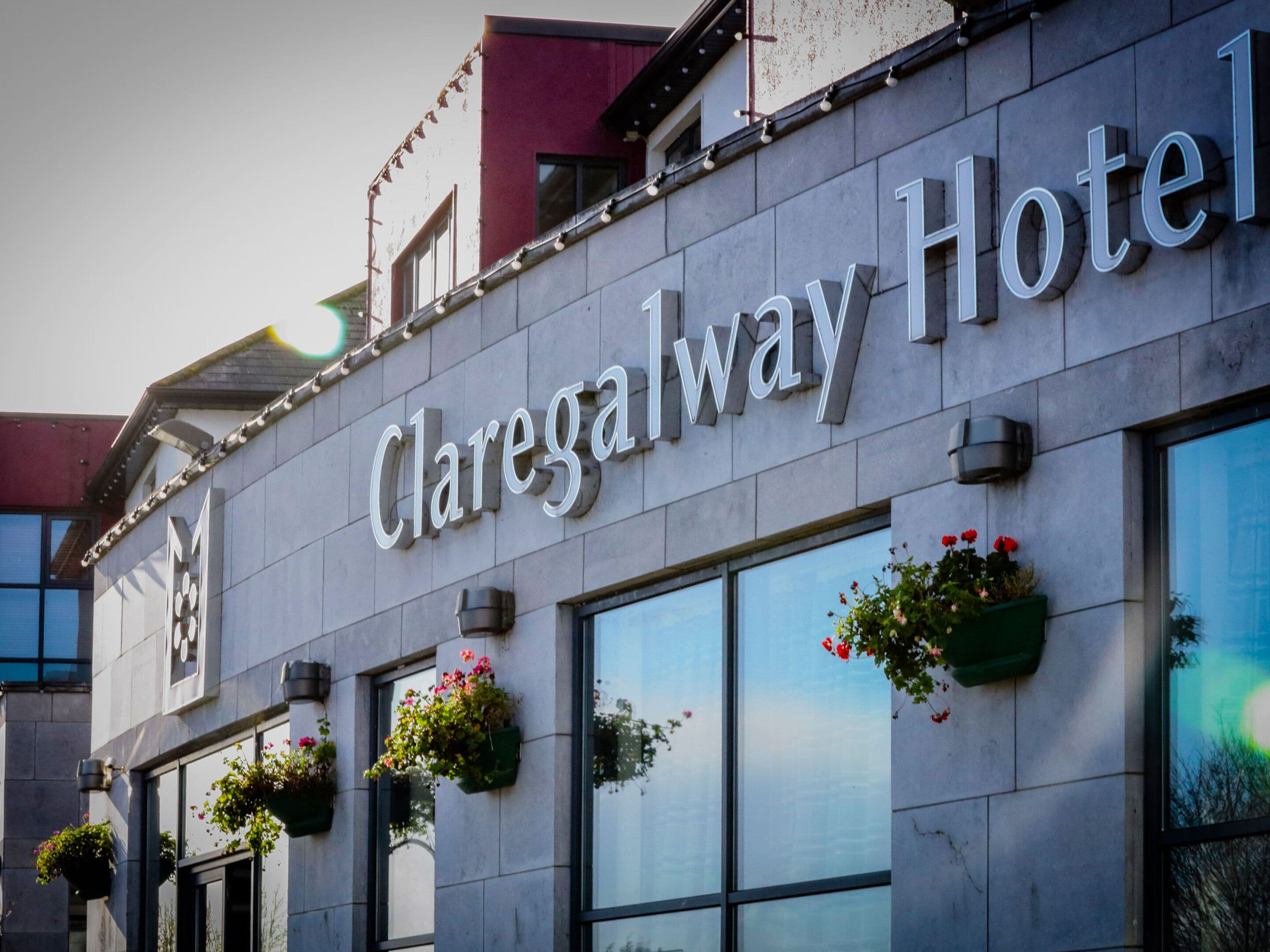Exterior del Hotel Claregalway, con un letrero, ventanas y macetas de flores.
