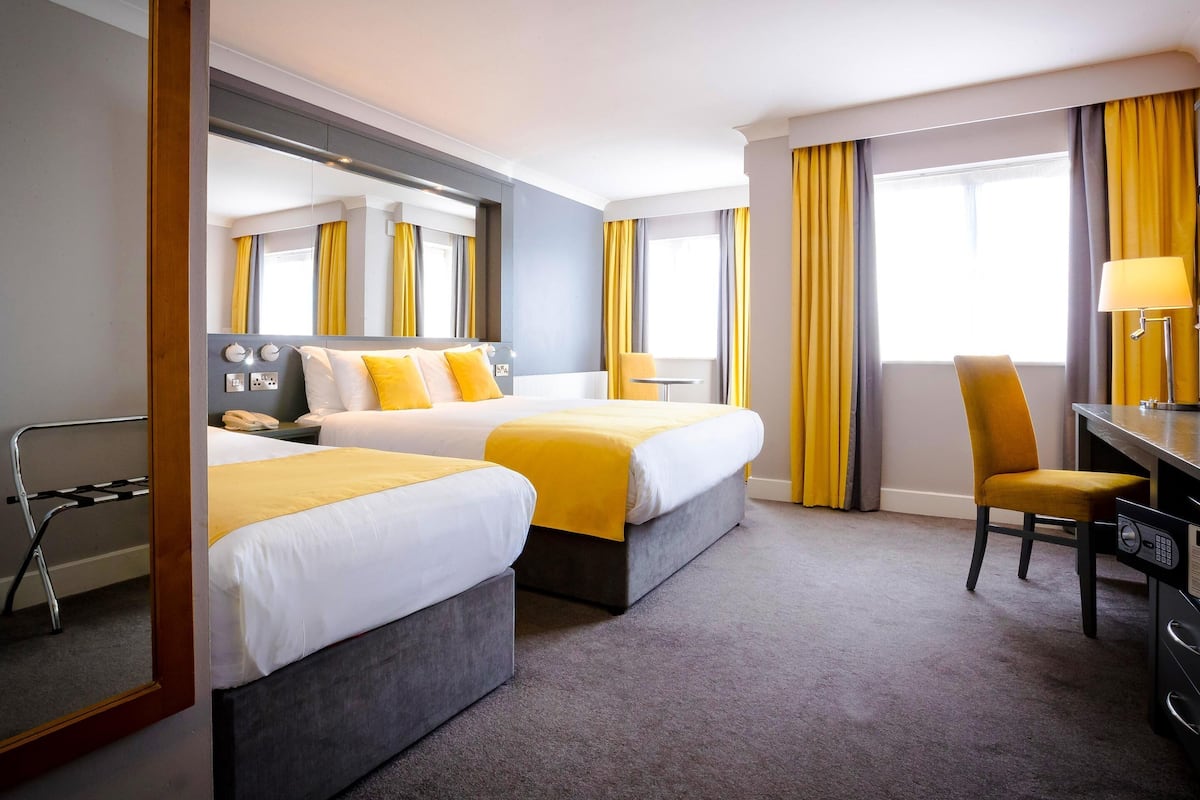 Une chambre d’hôtel avec deux lits, un bureau, une chaise, une lampe et un miroir.