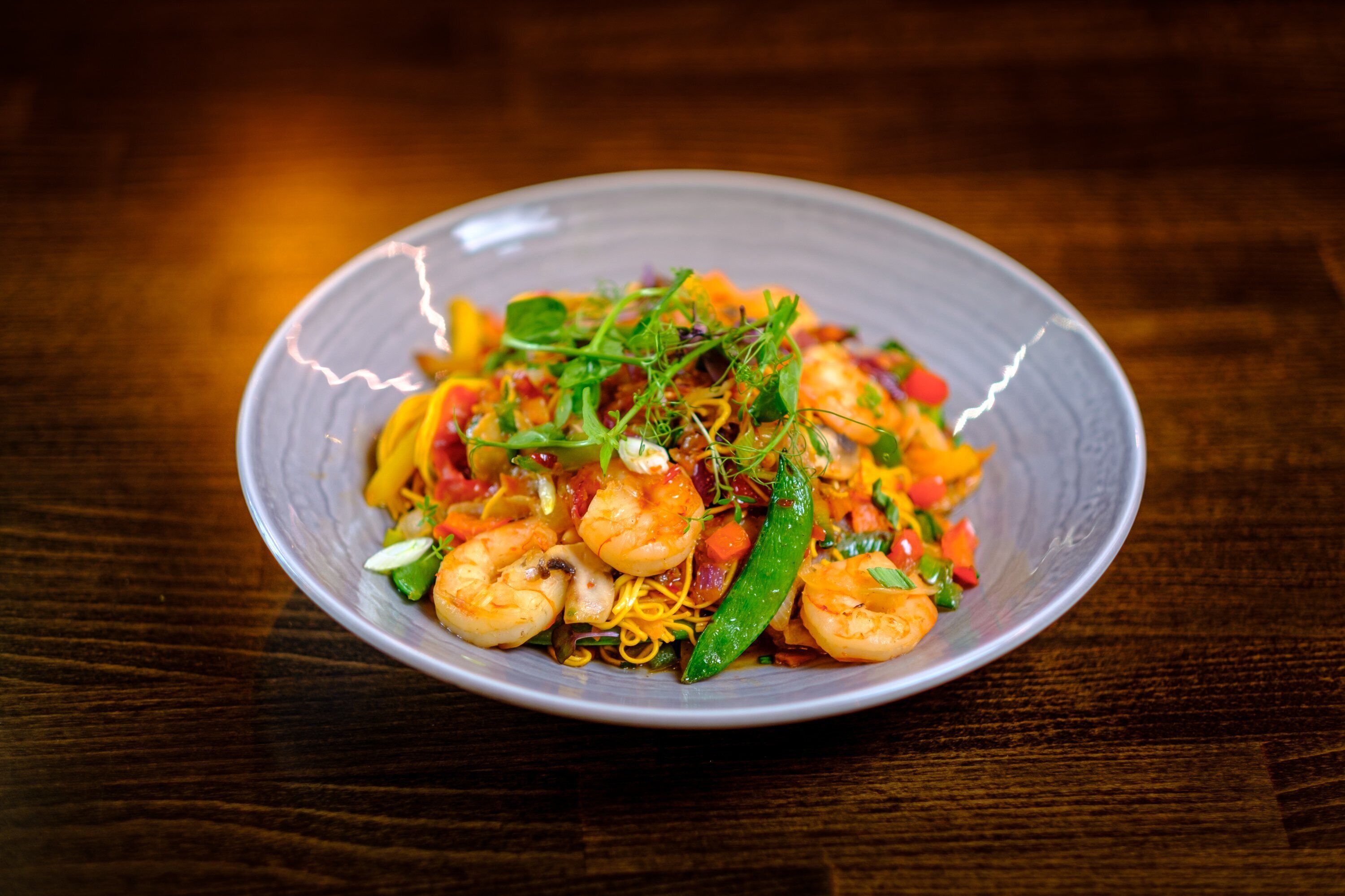 A plate of stir-fried shrimp and vegetables on a wooden table.