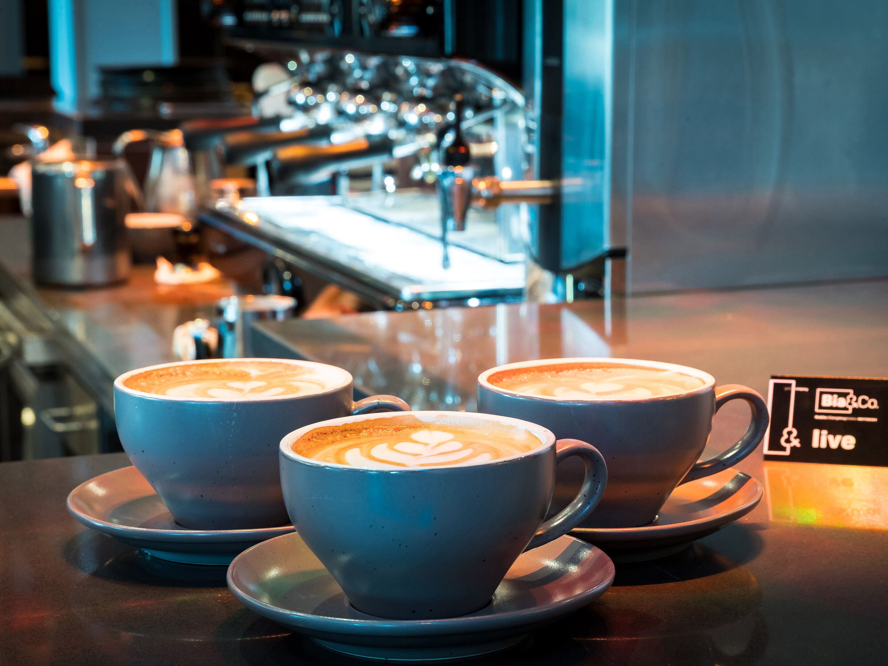 Three cups of coffee with latte art on a bar counter in a cafe.