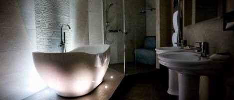 A modern bathroom with a large, bowl-shaped bathtub, a walk-in shower, and a pedestal sink.
