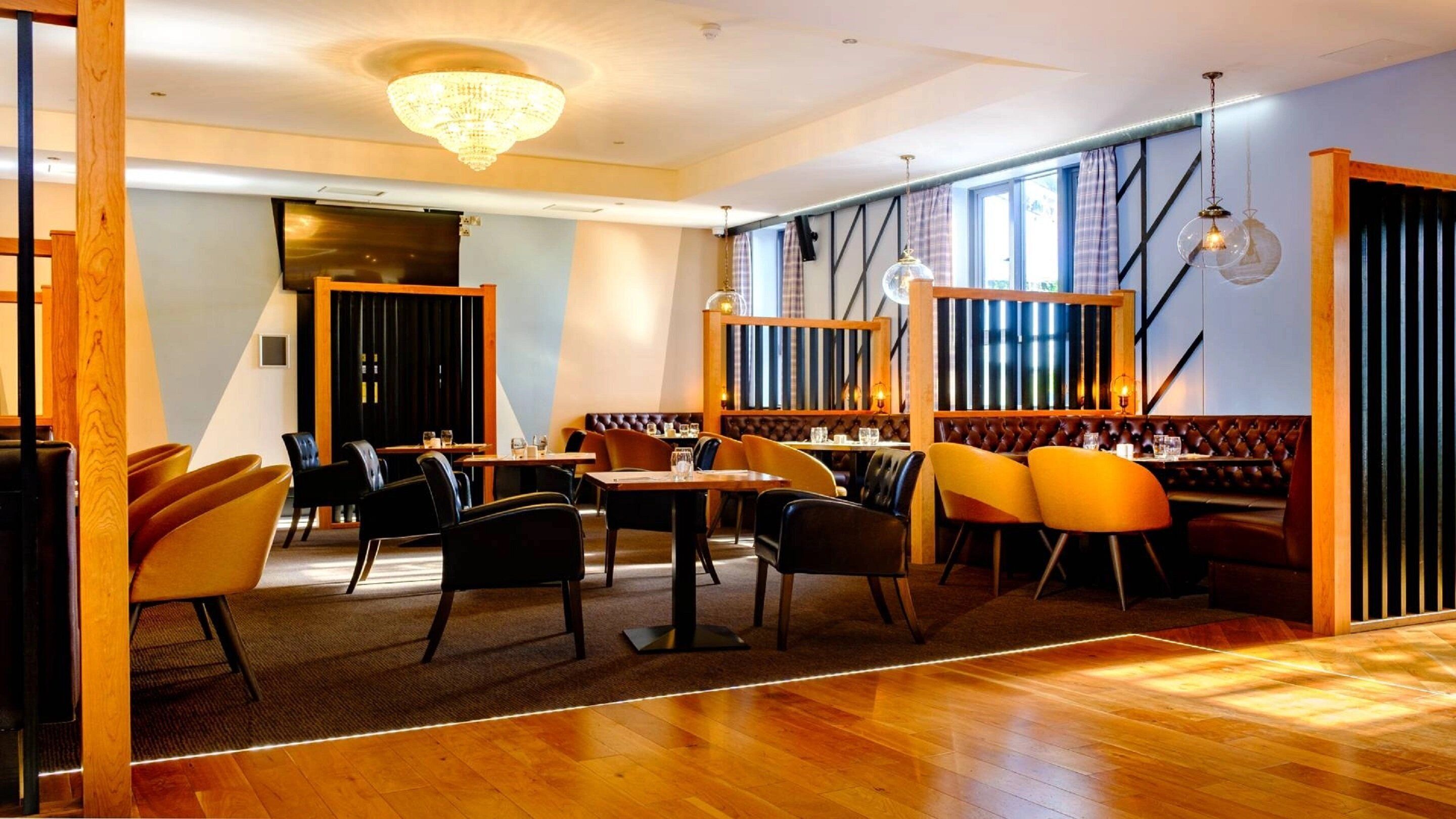 A modern restaurant with wooden flooring, leather booths, and a chandelier.