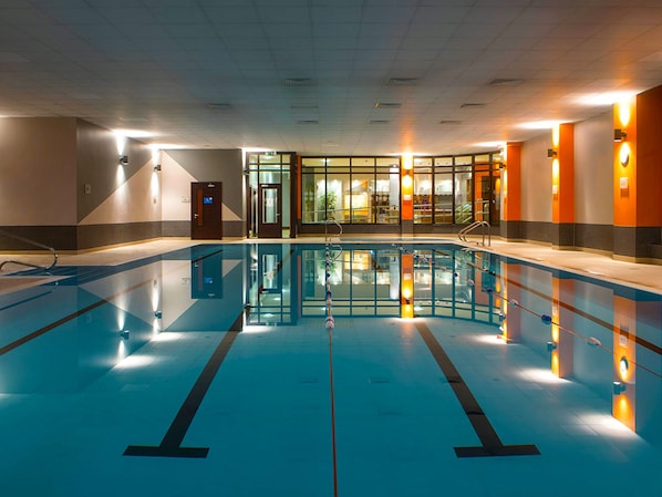 Una piscina interior con carriles delimitados, un muro de cristal y una puerta que da a un vestuario.