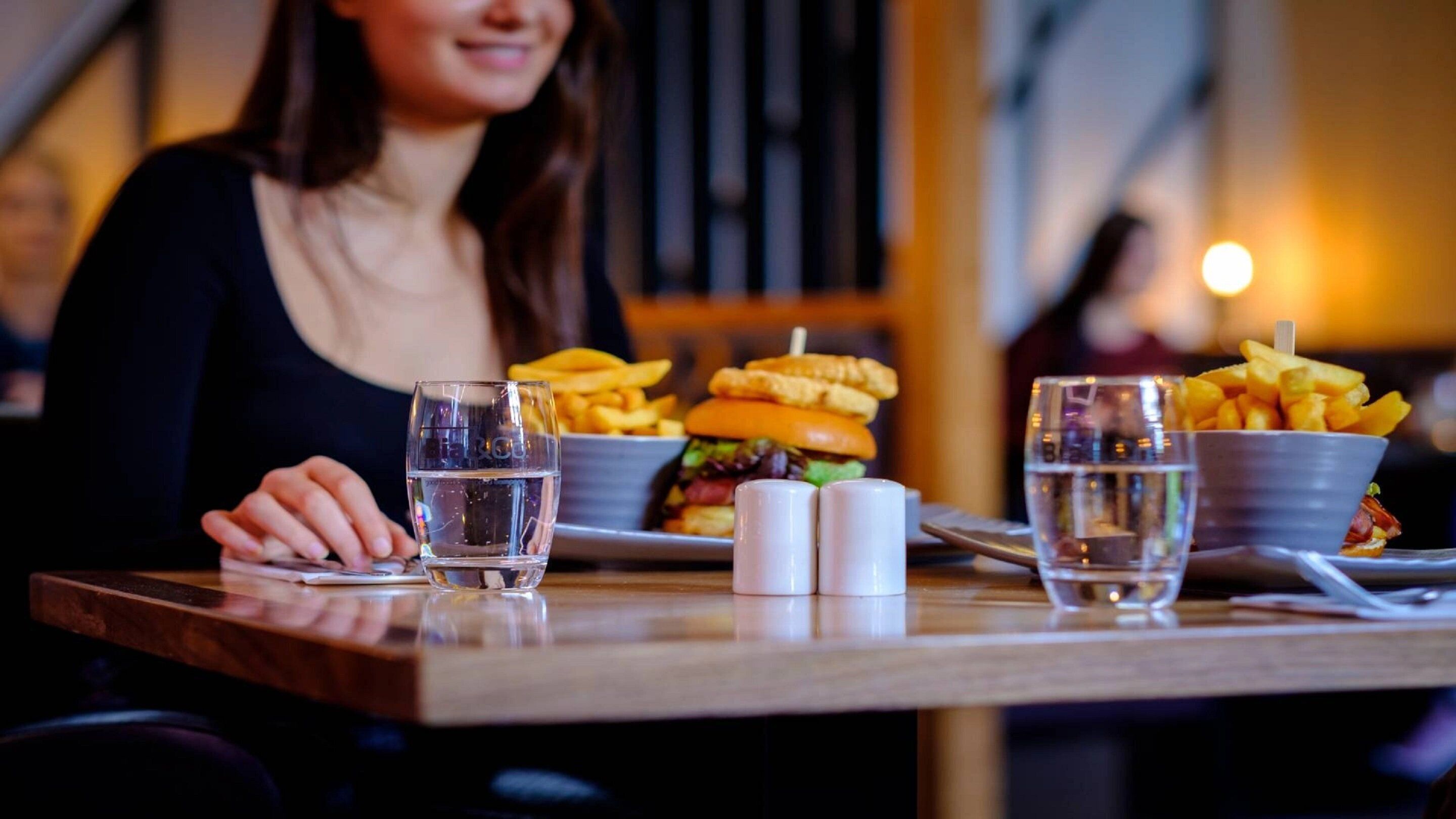 A dining table with a burger, fries, and two glasses of water.