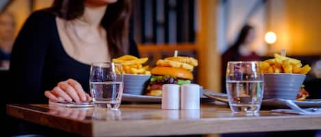 A dining table with a burger, fries, and two glasses of water.