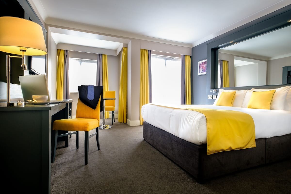 Une chambre d’hôtel avec un lit, un bureau avec un ordinateur portable, une chaise et un grand miroir.